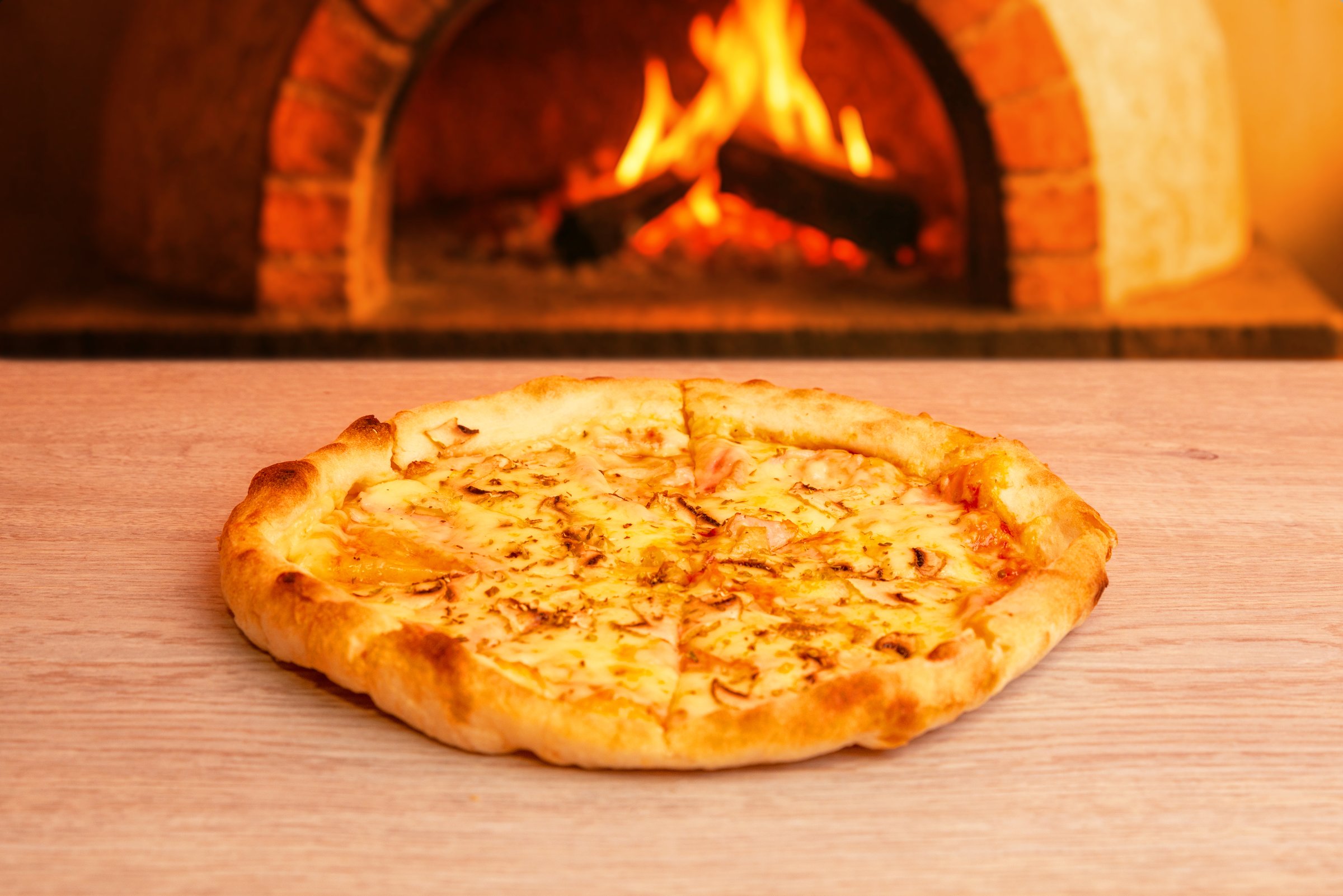 Tasty hot pizza in front of traditional brick wood-fired oven, cozy restaurant ambience with flame and warmth