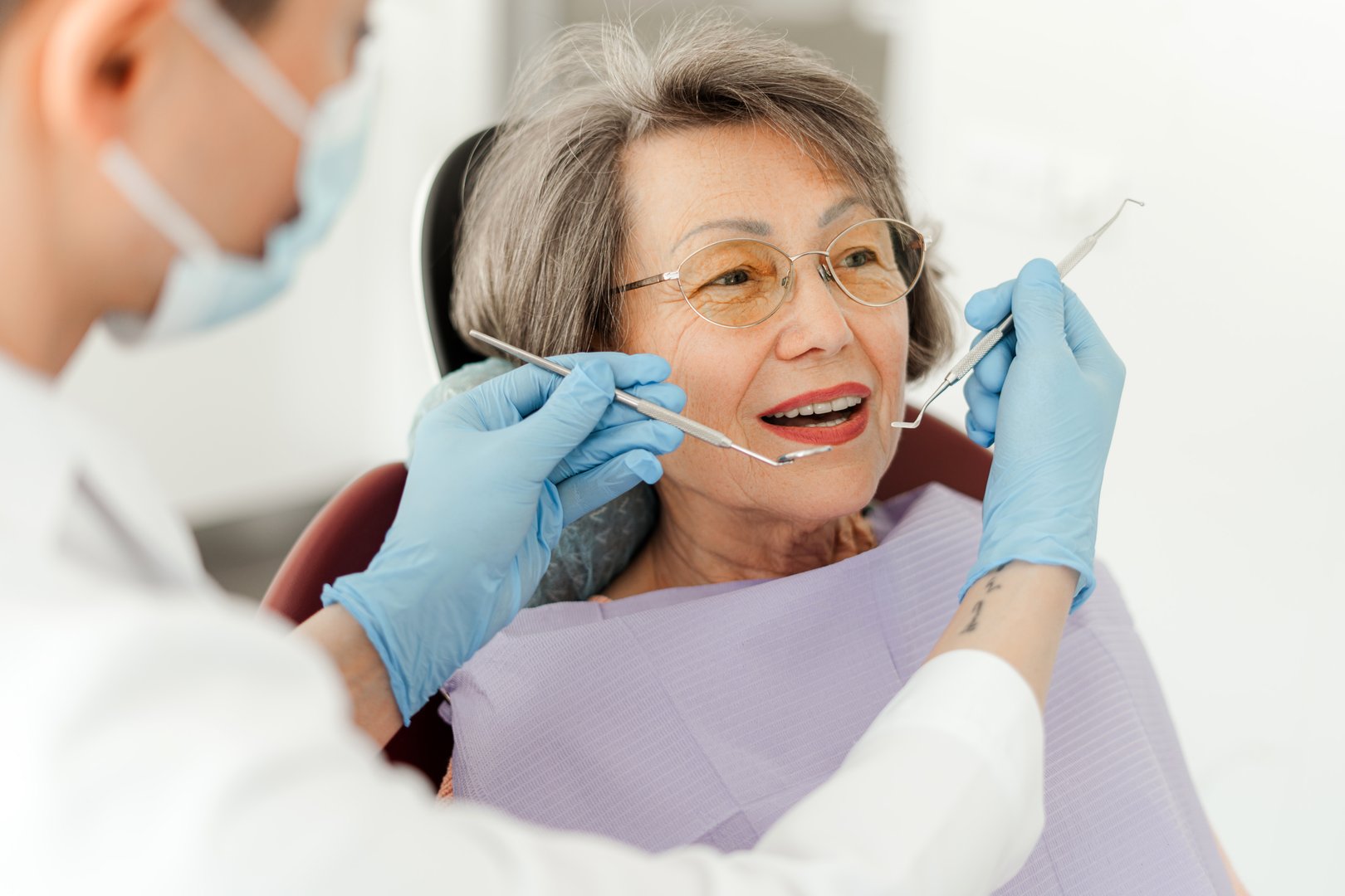 Attractive senior woman, patient sitting in dental chair with open mouth professional doctor holding dental tools, checking teeth. Concept of dental care, treatment teeth