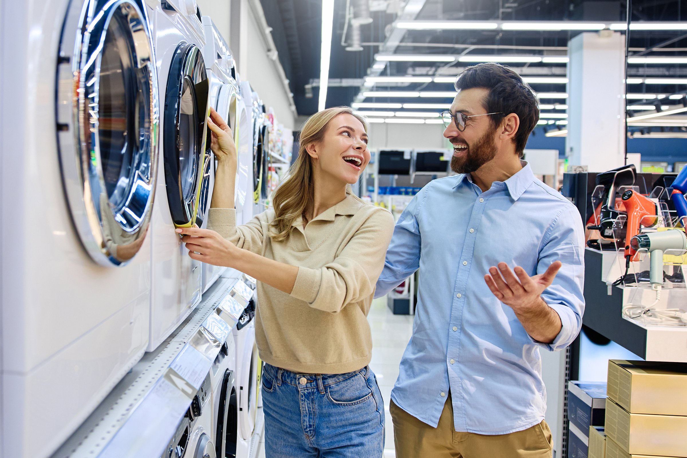 In a busy appliance store, a couple examines washing machines, reviewing energy efficiency labels and discussing options to find the best fit for their laundry needs and lifestyle