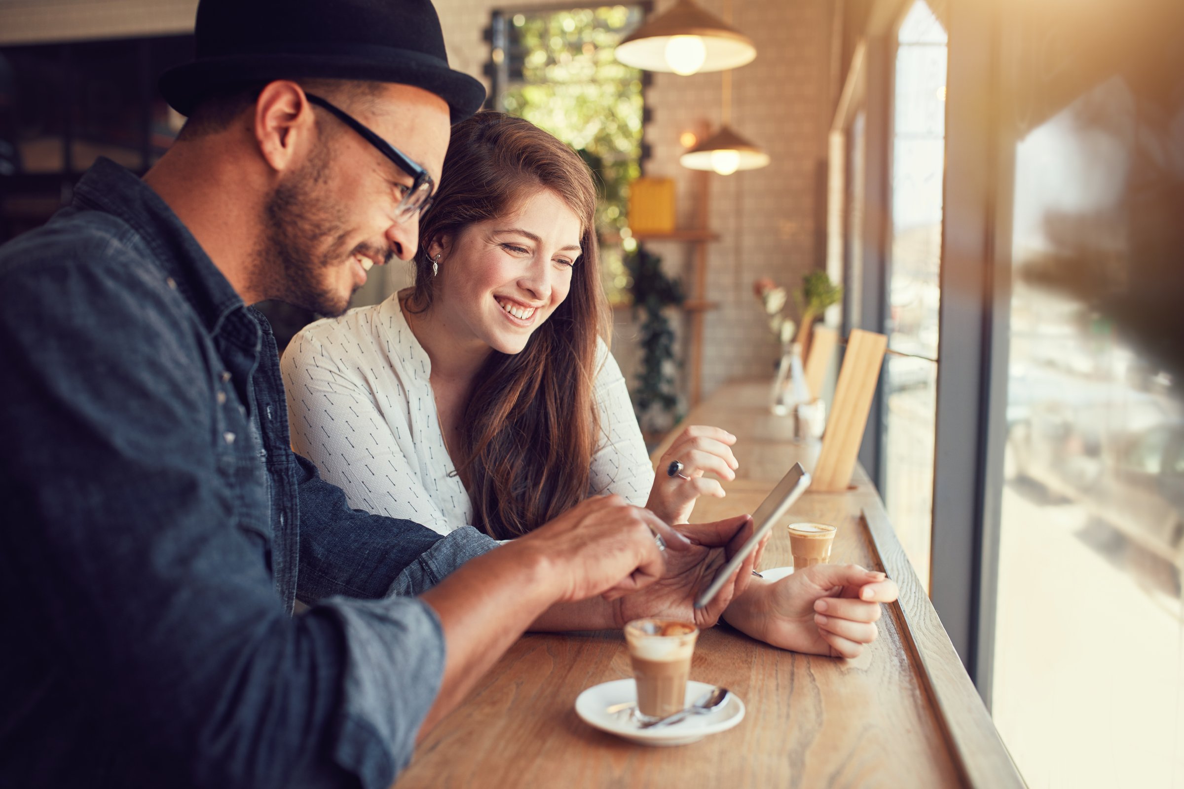 Happy couple in a coffee shop surfing internet on digital tablet. Young man and woman in a restaurant looking at touch screen computer.