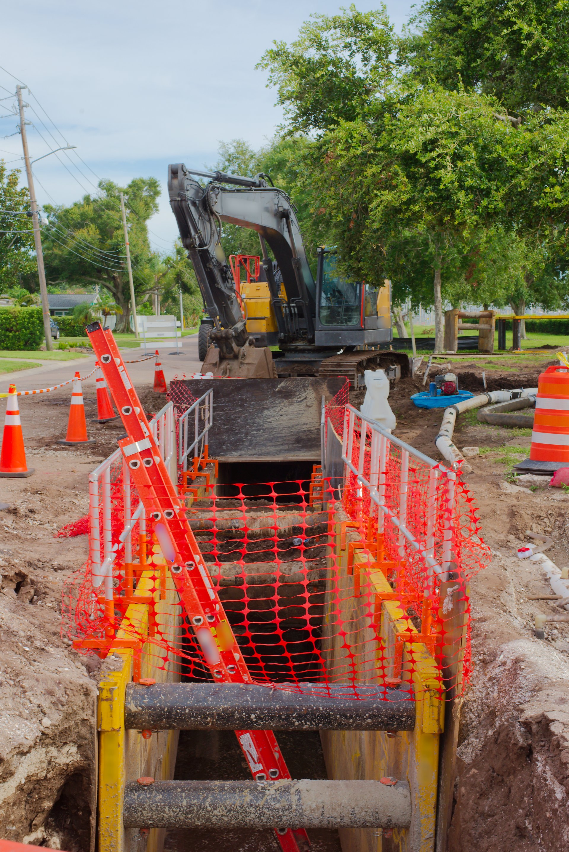 Construction site featuring safety cones, protective mesh fencing around a trench, and pipeline equipment, highlighting precaution and progress in urban infrastructure development.