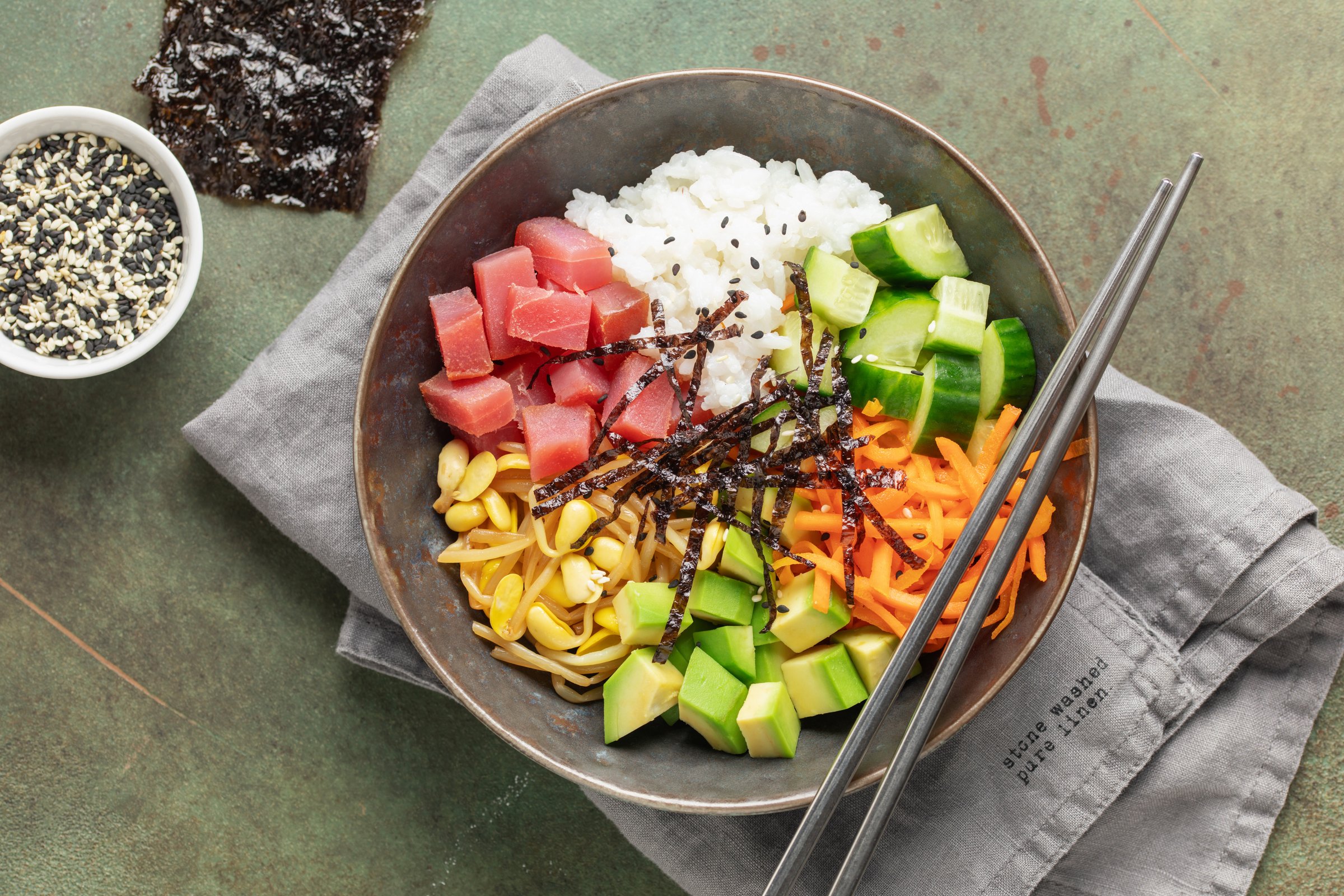 A traditional dish of Hawaiian cuisine. Poke bowl with tuna and vegetables in a bowl on the table. Top view