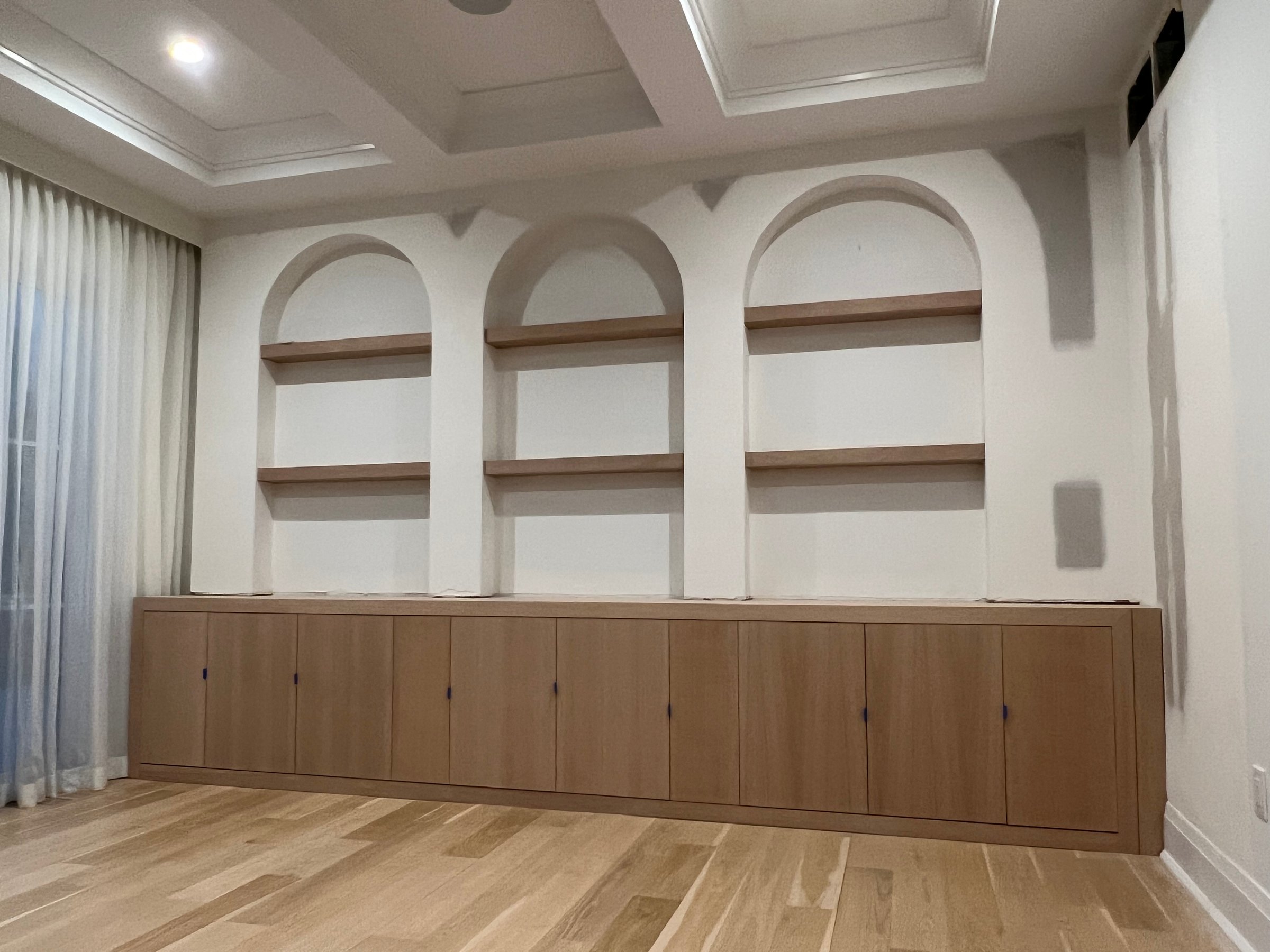Built-in wooden shelves with closed cabinets below, set against a white wall with recessed arches.