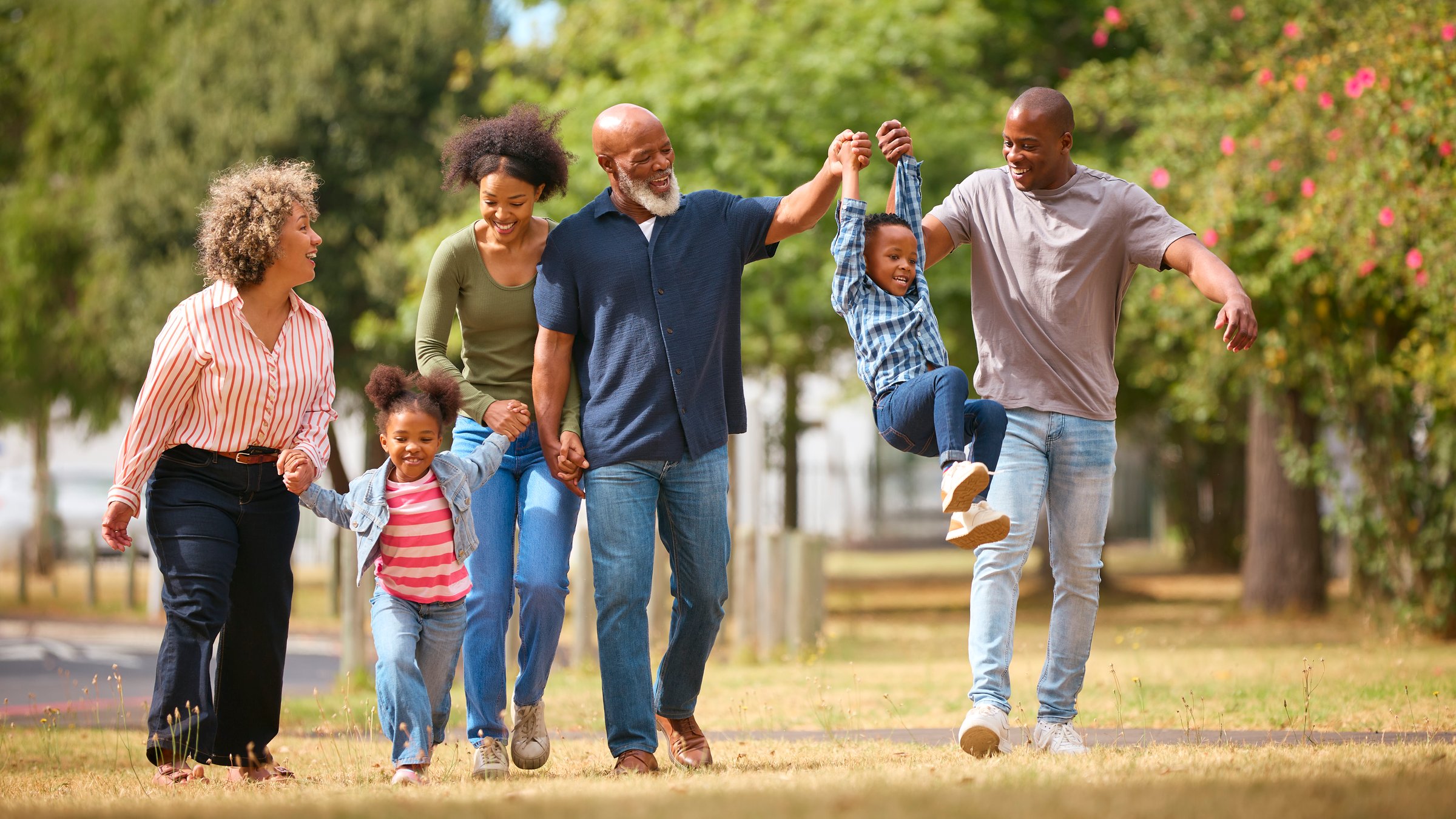 Three Generation Family Walking Outdoors Laughing And Playing And Swinging Grandchildren Between Them