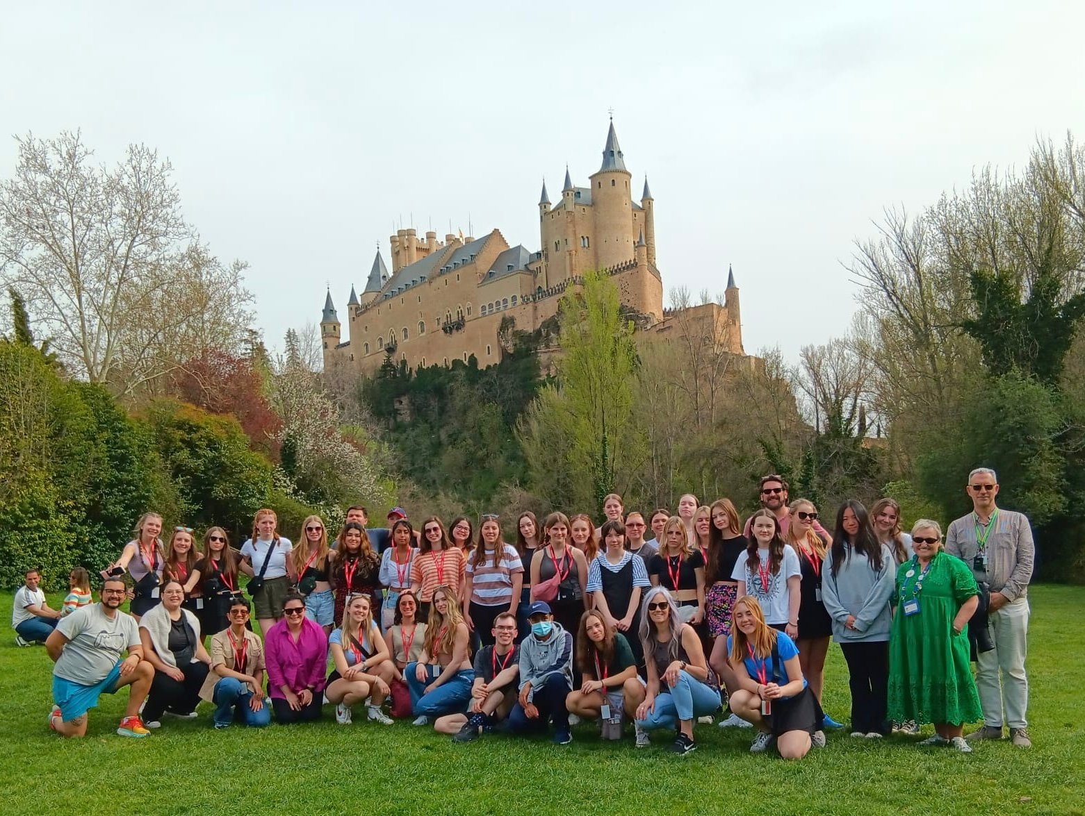 A group of people posing on a grassy field with a large historic castle in the background on a clear day.