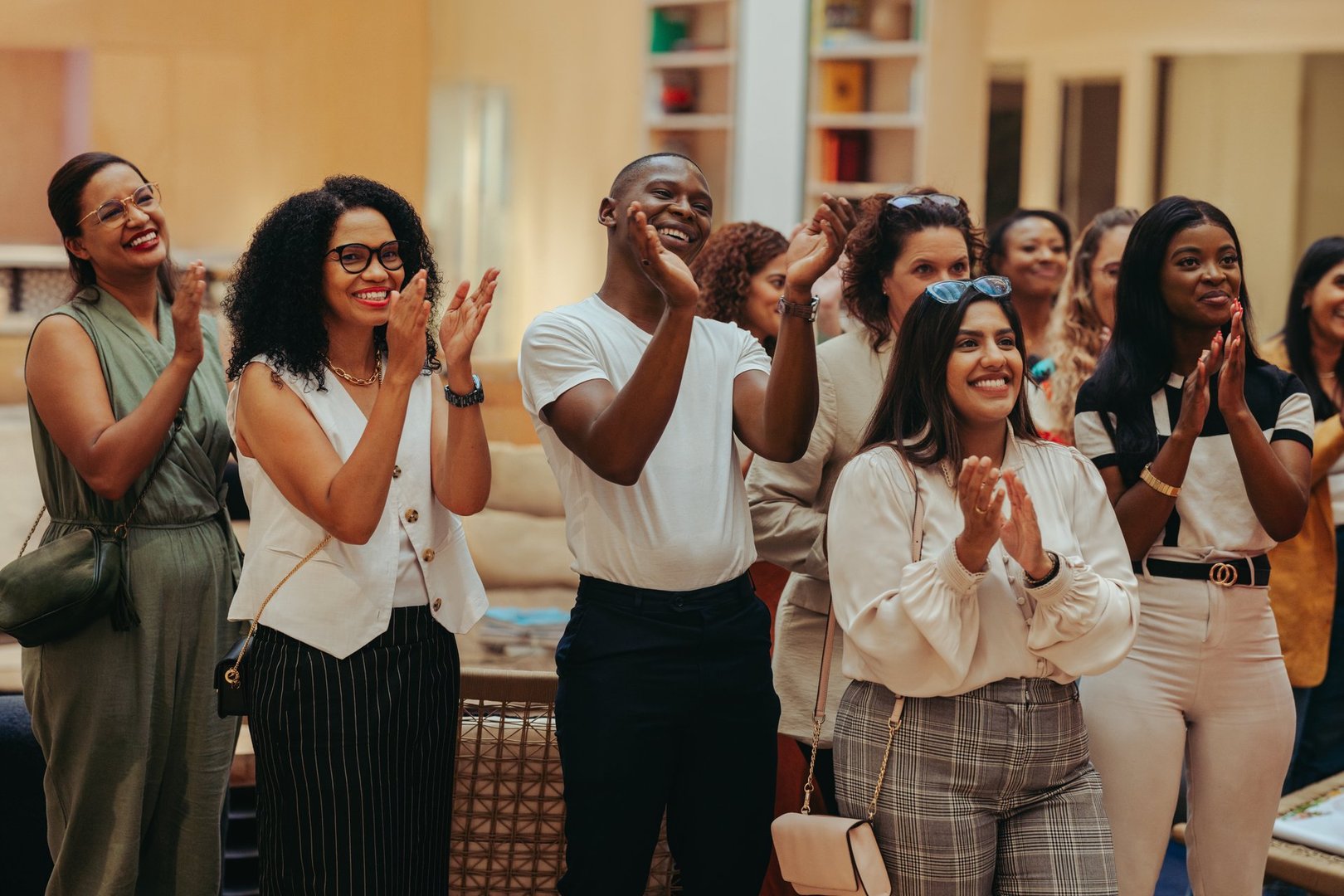 A diverse group of happy employees clapping and smiling in an office setting. The atmosphere is joyful and inclusive, with individuals from various backgrounds sharing in positive engagement.
