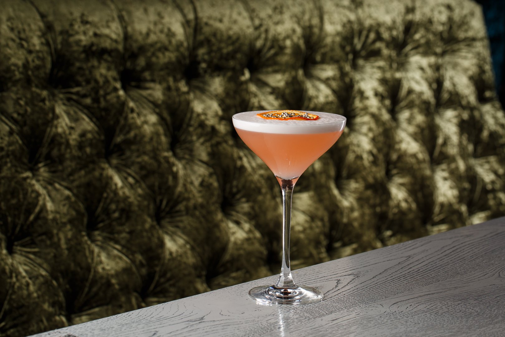 Orange Clover Club Cocktail in Coupe Glass with Layer of Foam and orange chips Garnish isolated on dark Background