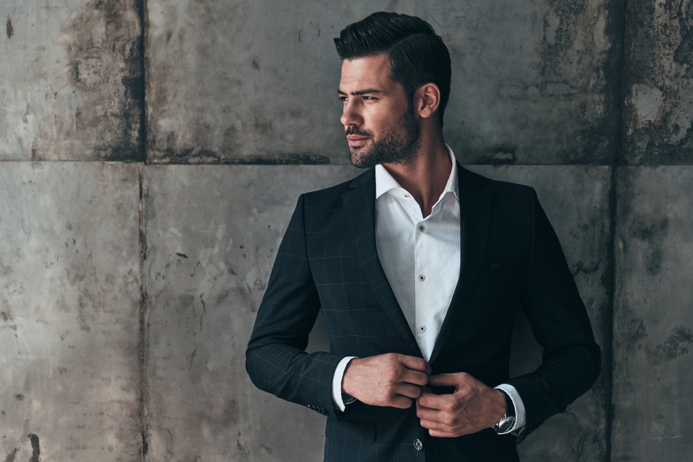 Handsome young man in suit looking away and adjusting his jacket while standing indoors