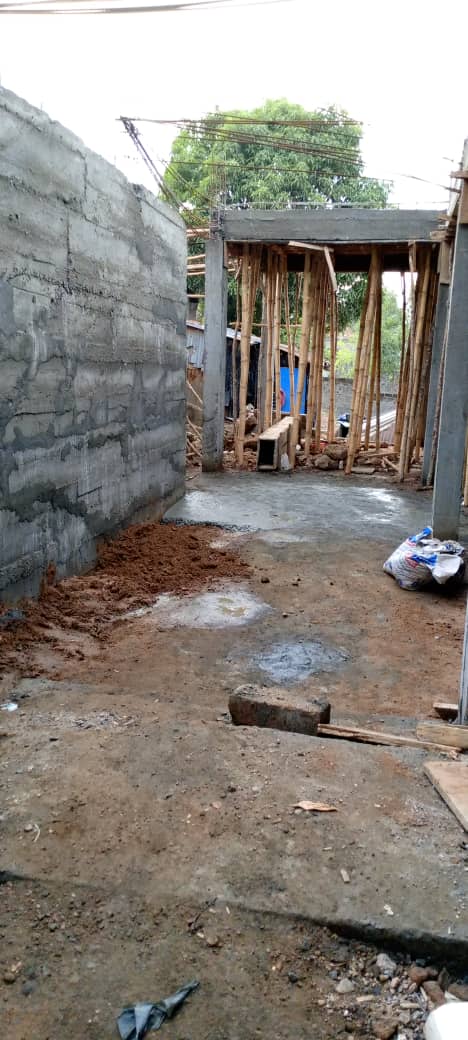 Reinforced concrete foundation with steel rebar grid at a construction site, surrounded by a stone wall and building materials.