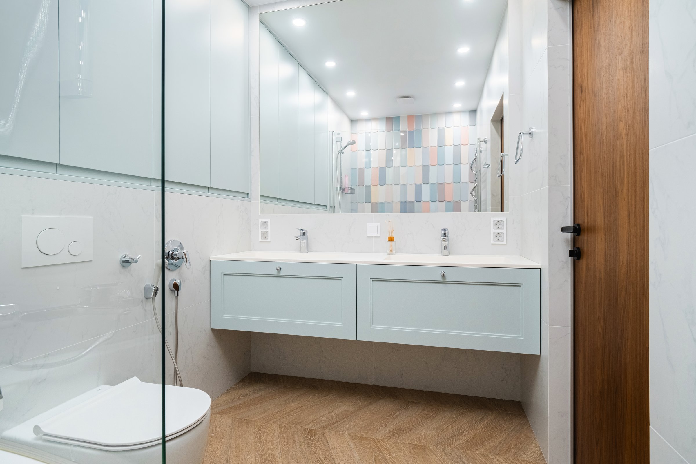 A sleek bathroom showcases modern design elements, with a glass shower enclosure, light blue cabinetry, and elegant wooden flooring, perfectly blending style and functionality.
