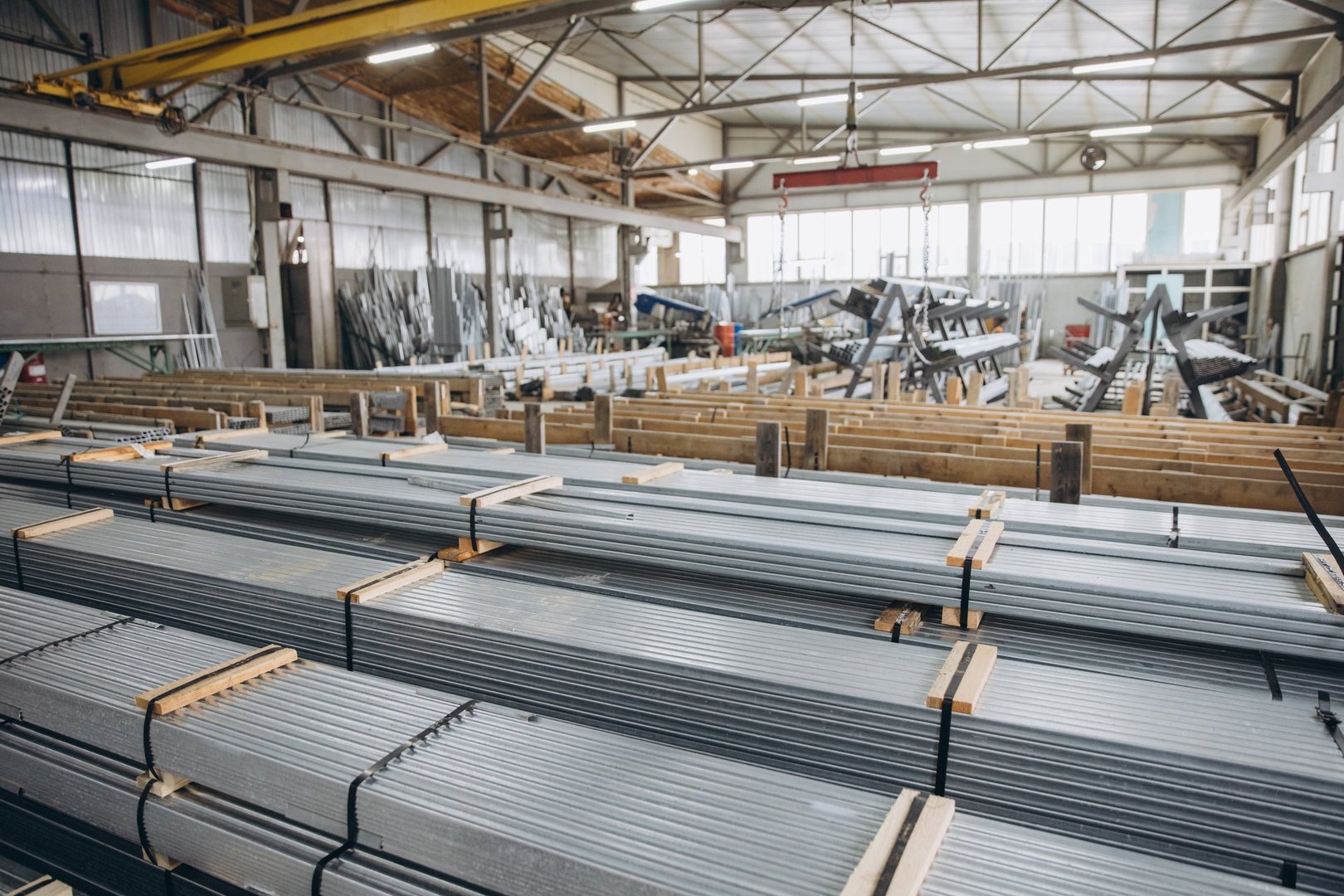 Metal profiles stacked on wooden pallets in a factory, ready for the production of windows and doors