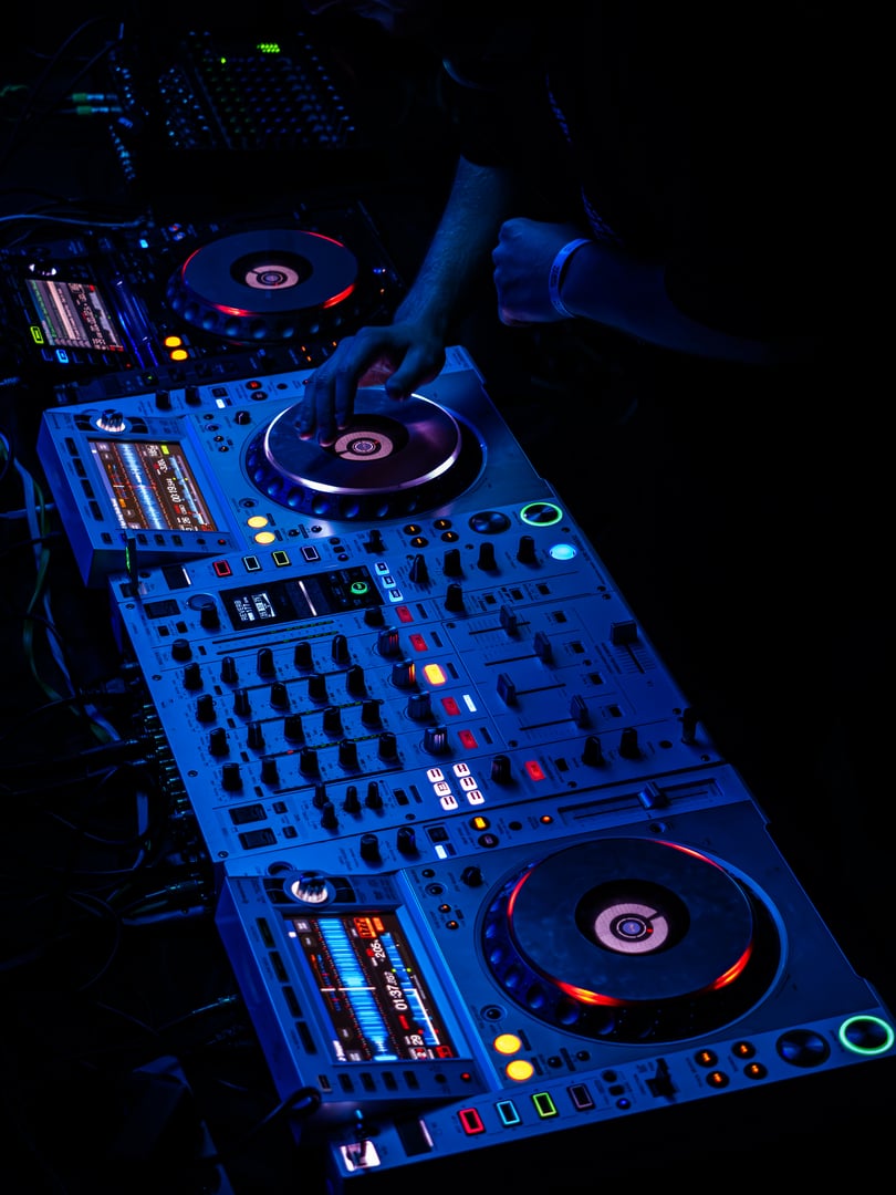 DJ setup with glowing turntables in blue light, creating an atmospheric scene of electronic music performance at a club or festival.