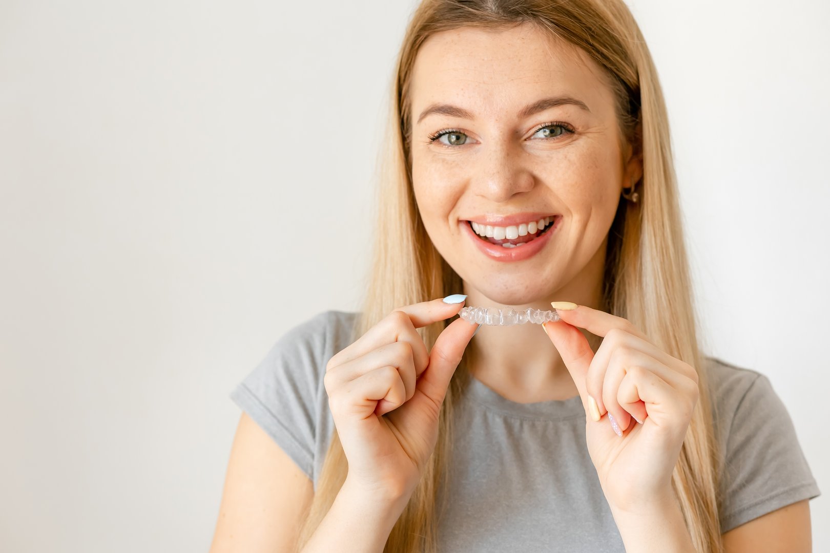 Smiling young woman over white background holding an invisible braces aligner recommending this new treatment. Dental healthcare concept.
