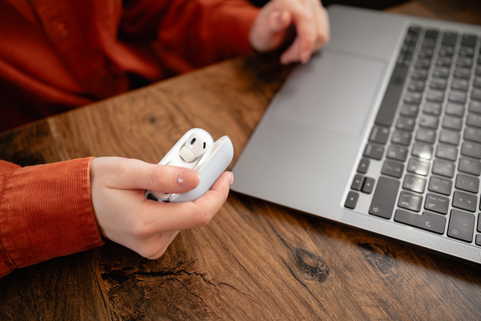 Freelancer working in a cafe. Close-up of female hands holding a case with wireless earbuds near a laptop. Copy space