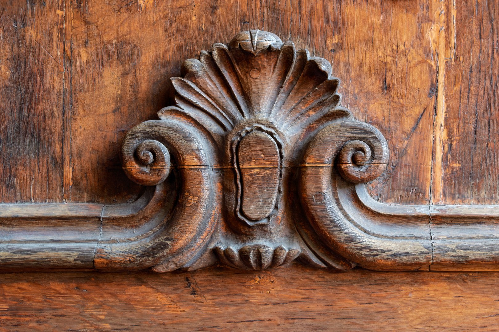 Ornate vintage wood carving with rich texture and intricate symmetrical details decorates an old brown wooden surface, evoking history.