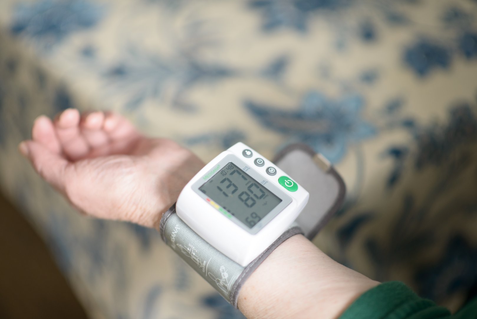 An elderly woman taking her blood pressure with a digital monitor