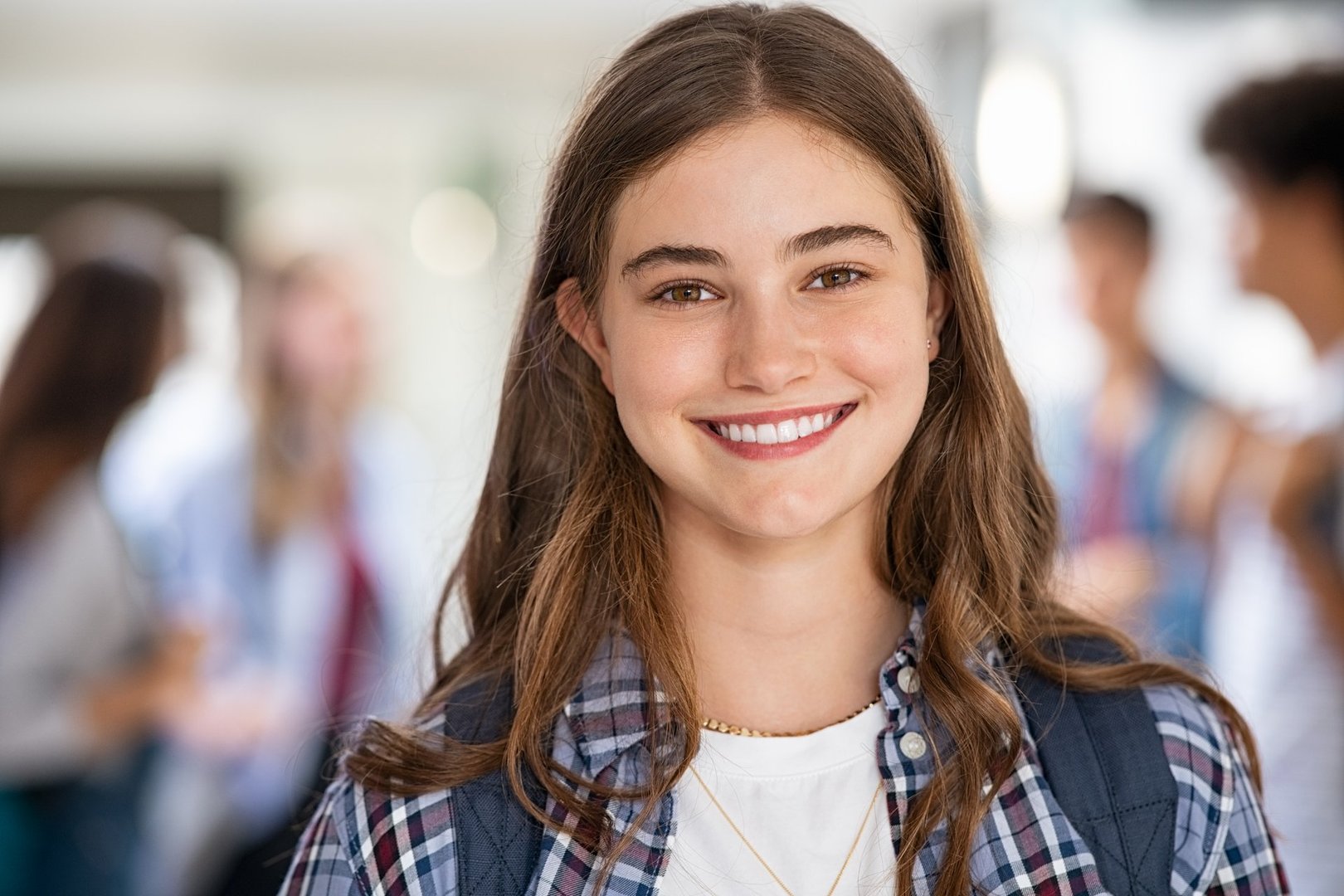 Portrait of beautiful girl standing in college campus and looking at camera. University young woman with backpack smiling. Satisfied and proud student girl standing in high school hallway.
