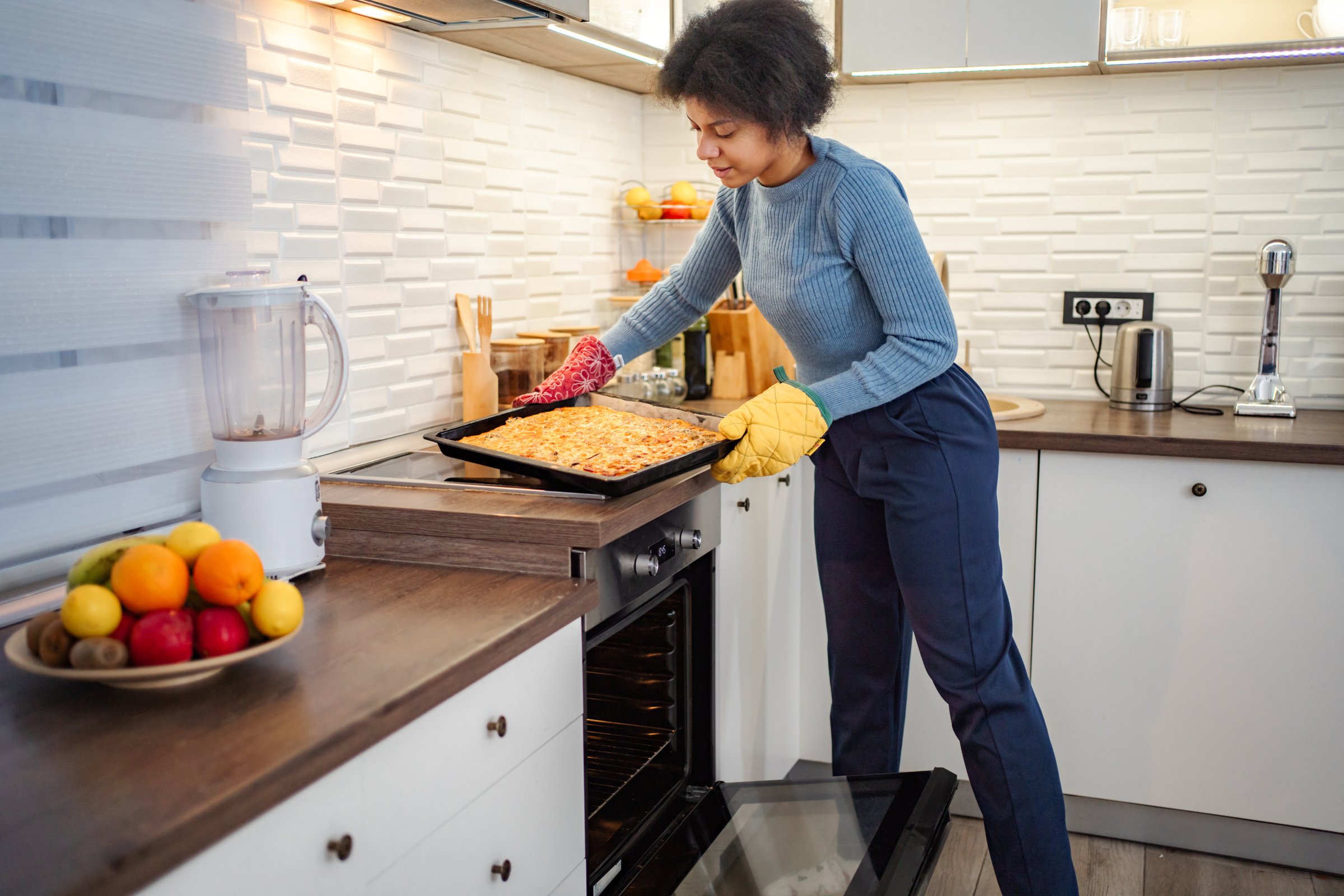 Young adult woman putting tray of baking pastry into oven