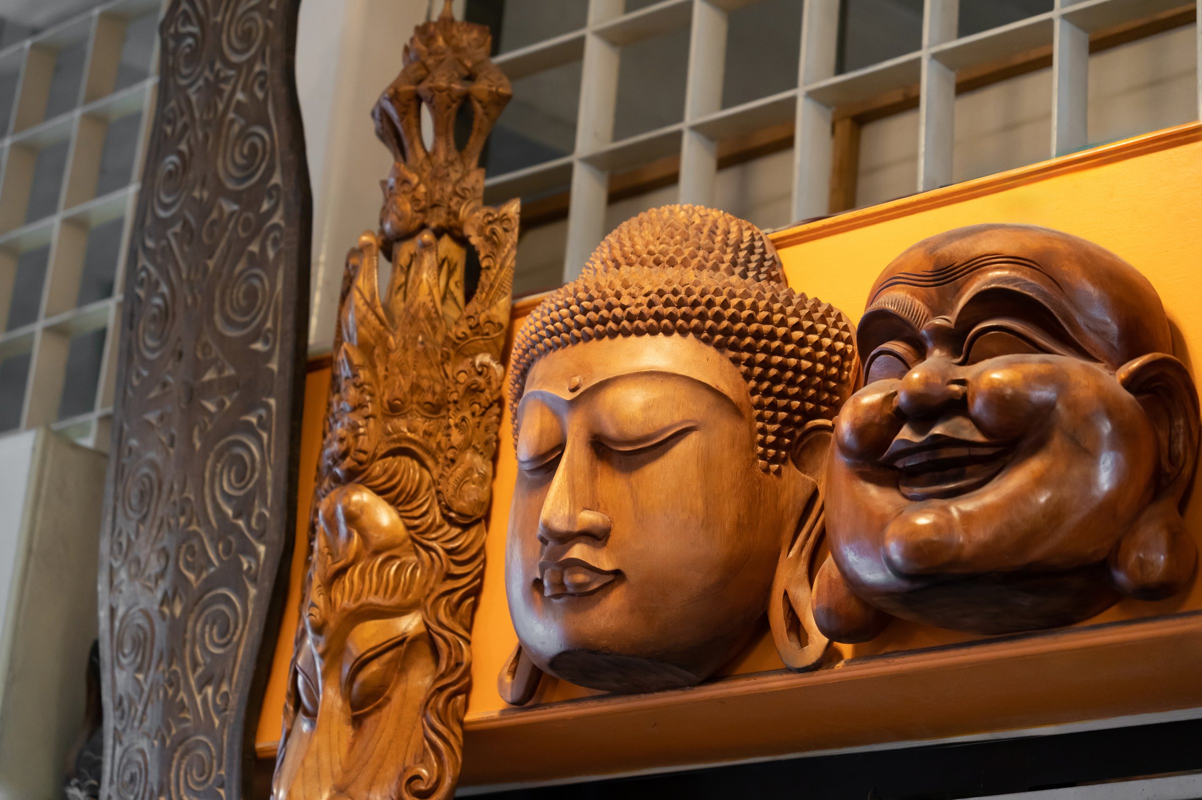 Close-up of intricately carved wooden faces, depicting a serene Buddha and cheerful Laughing Buddha, showcased in a decorative setting. Perfect for Asian culture, spirituality, and craft art themes.