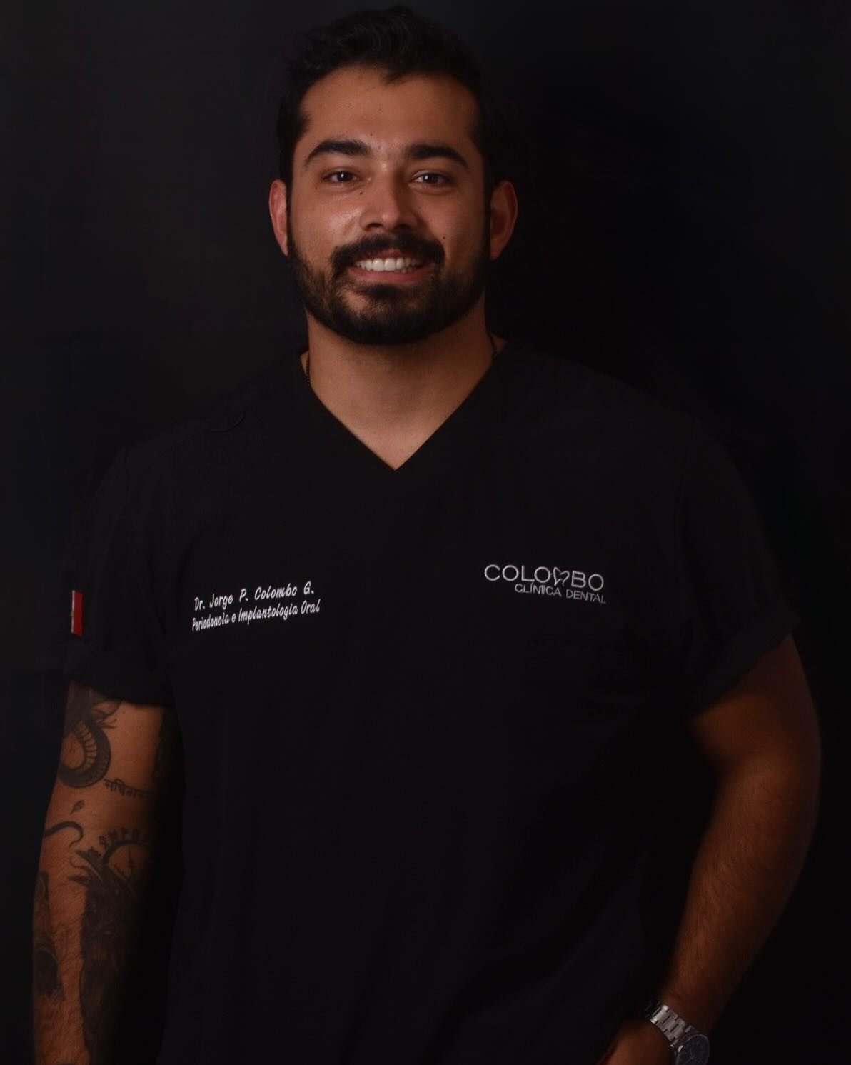 Smiling man in a black dental clinic uniform, standing against a dark background.