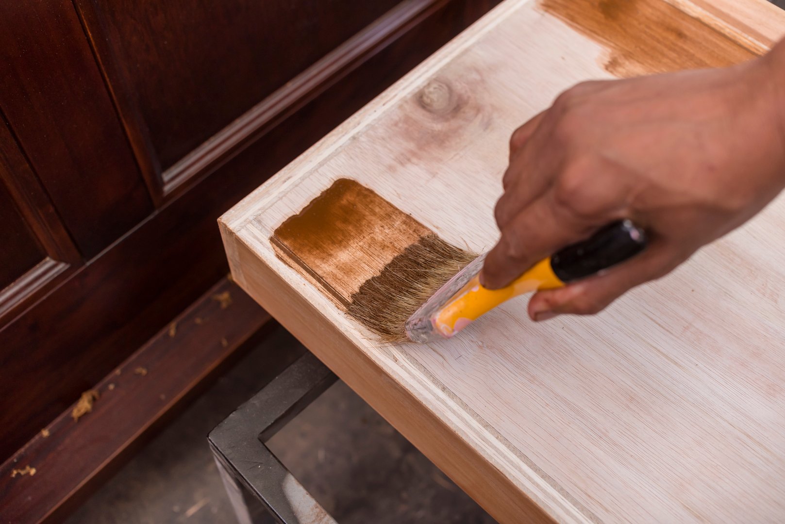 A carpenter applying varnish to a cabinet drawer with a paintbrush. First coating. At a furniture and woodworking shop.