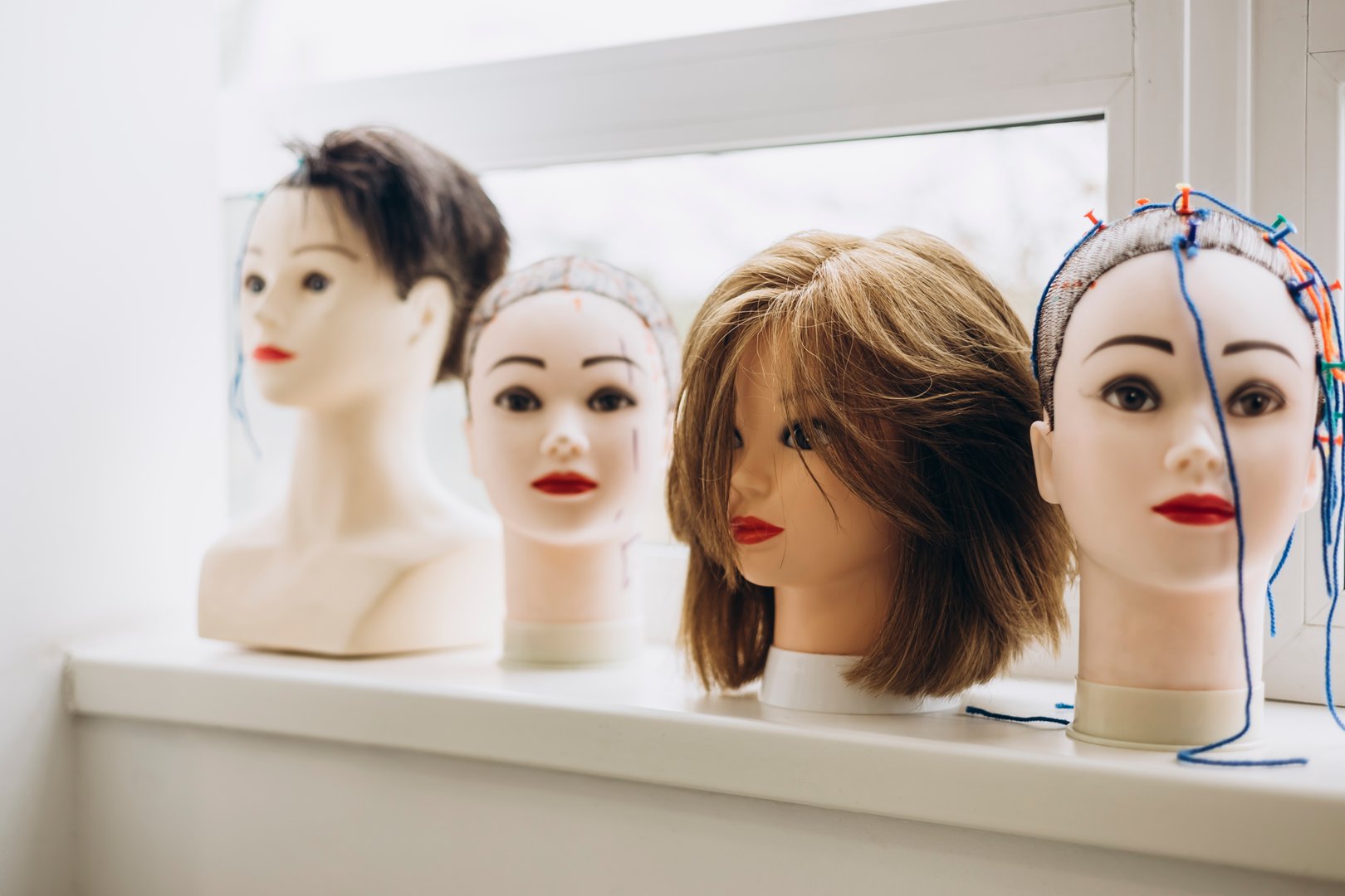 Multiple mannequin heads used for practicing haircuts and hairstyles in a professional hairdressing school. Educational setup for beauty students learning salon techniques.