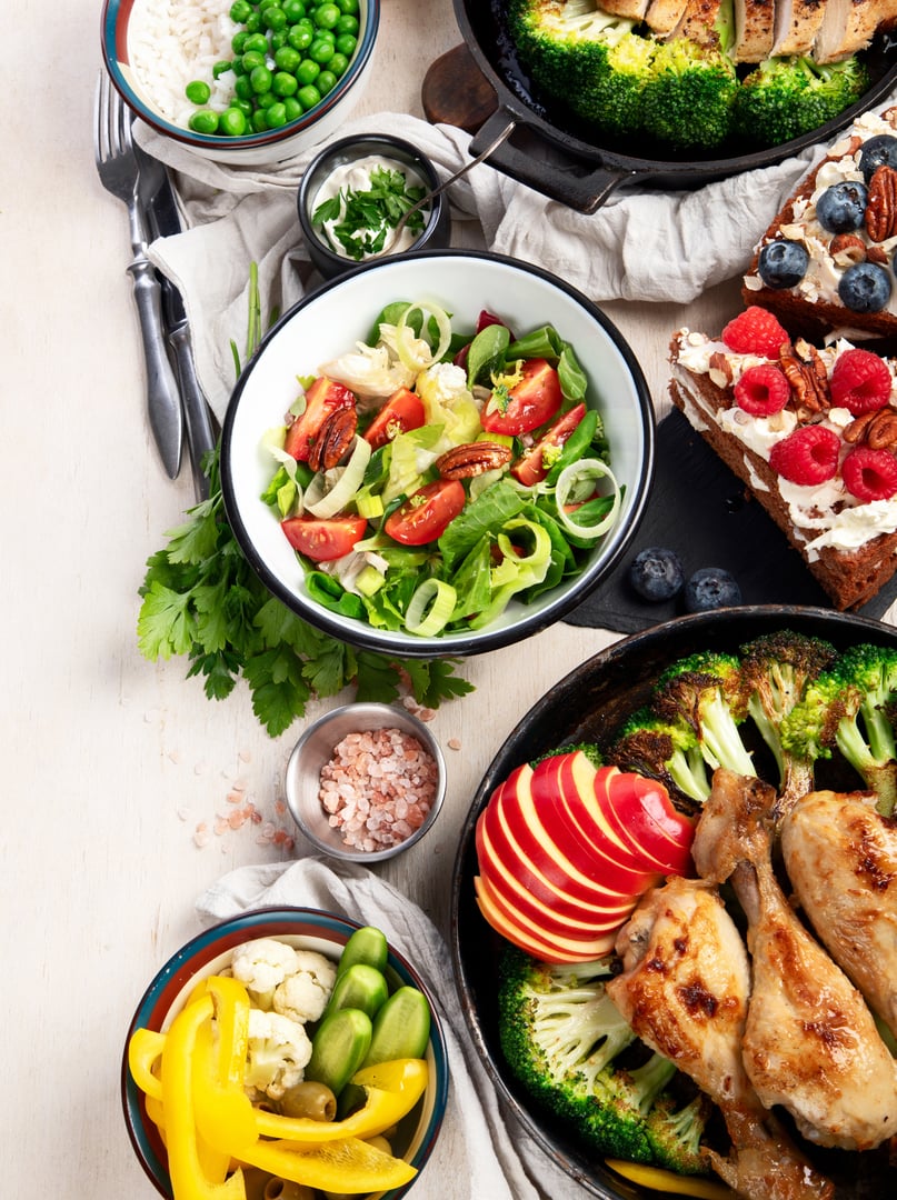 Variety of plates and bowls with green vegetables, chicken and fresh salads on a light background. Healthy food concept. Top view. Copy space.