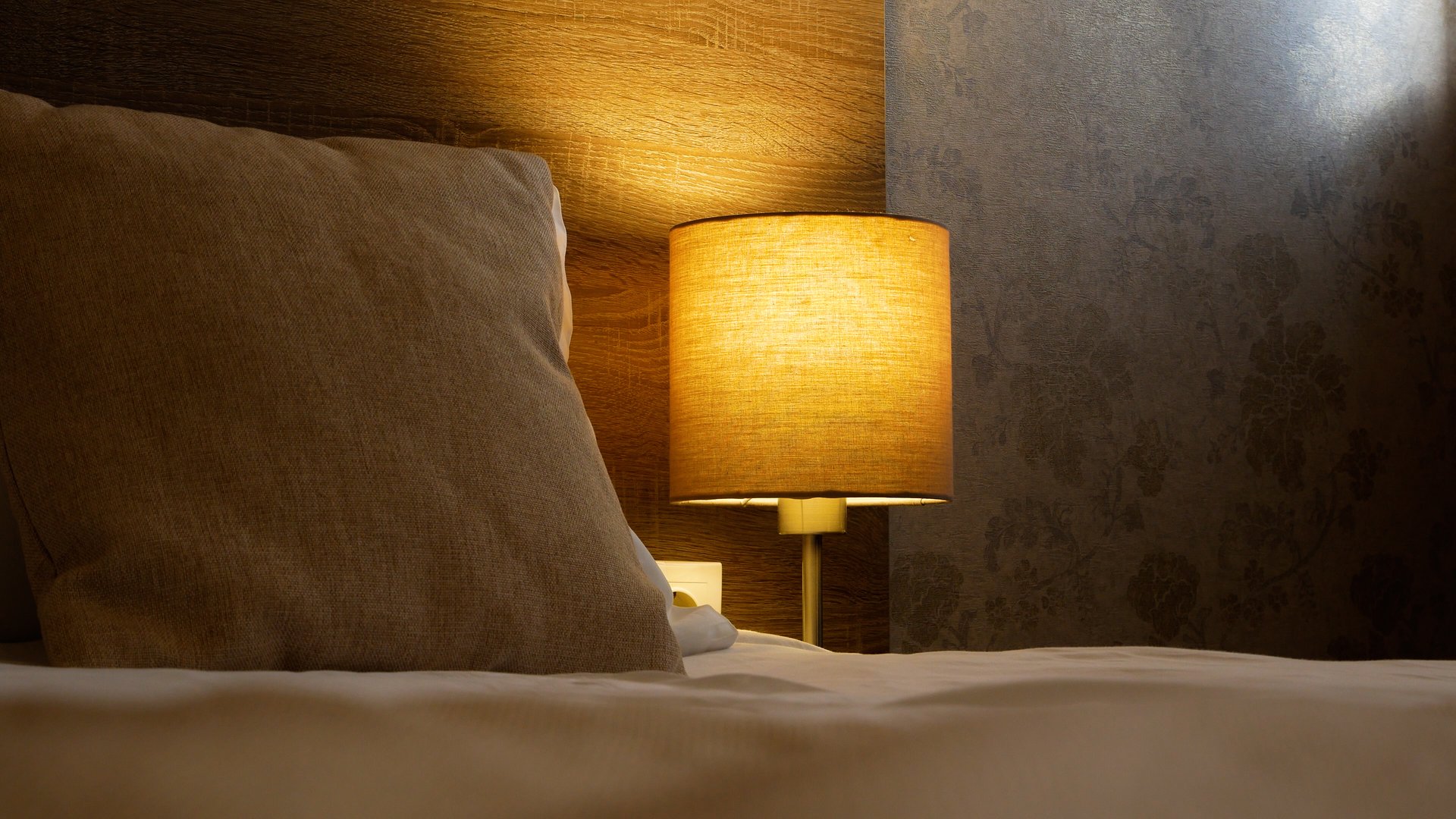 Bedroom interior. A bed with a pillow, next to it is a lamp on. Cozy lamp atmosphere on a quiet evening.