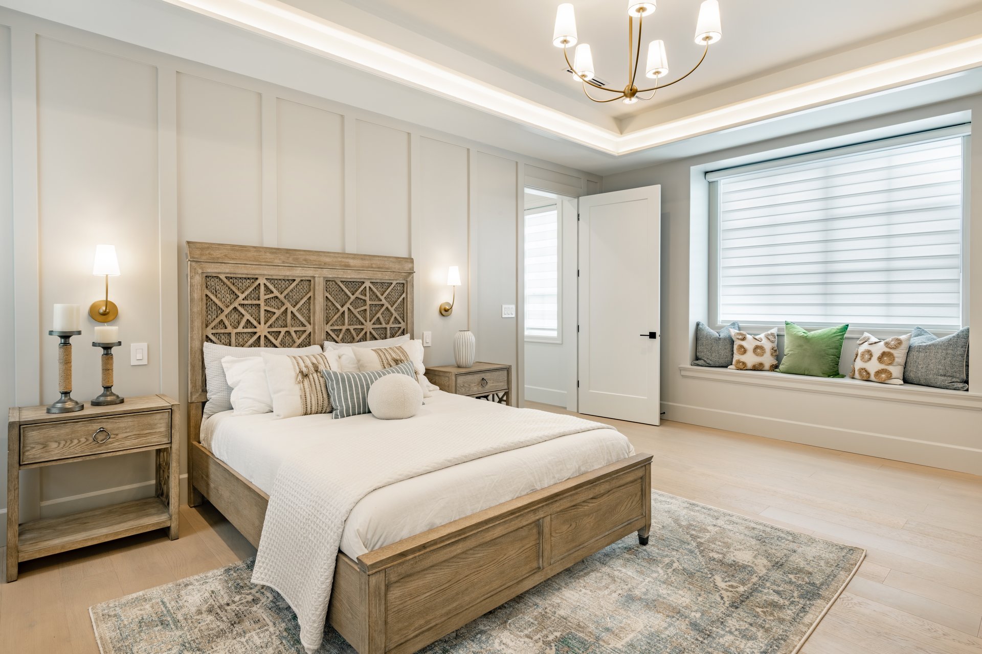 a very large and spacious primary master bedroom with queen sized wooden bed with carved headboard hardwood flooring area rug art work orange arm chair and houseplants