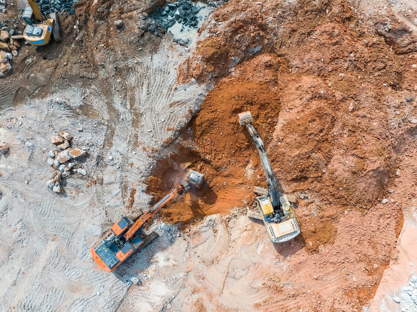 Large tracked excavator with hydraulic hammer breaks asphalt at a construction site