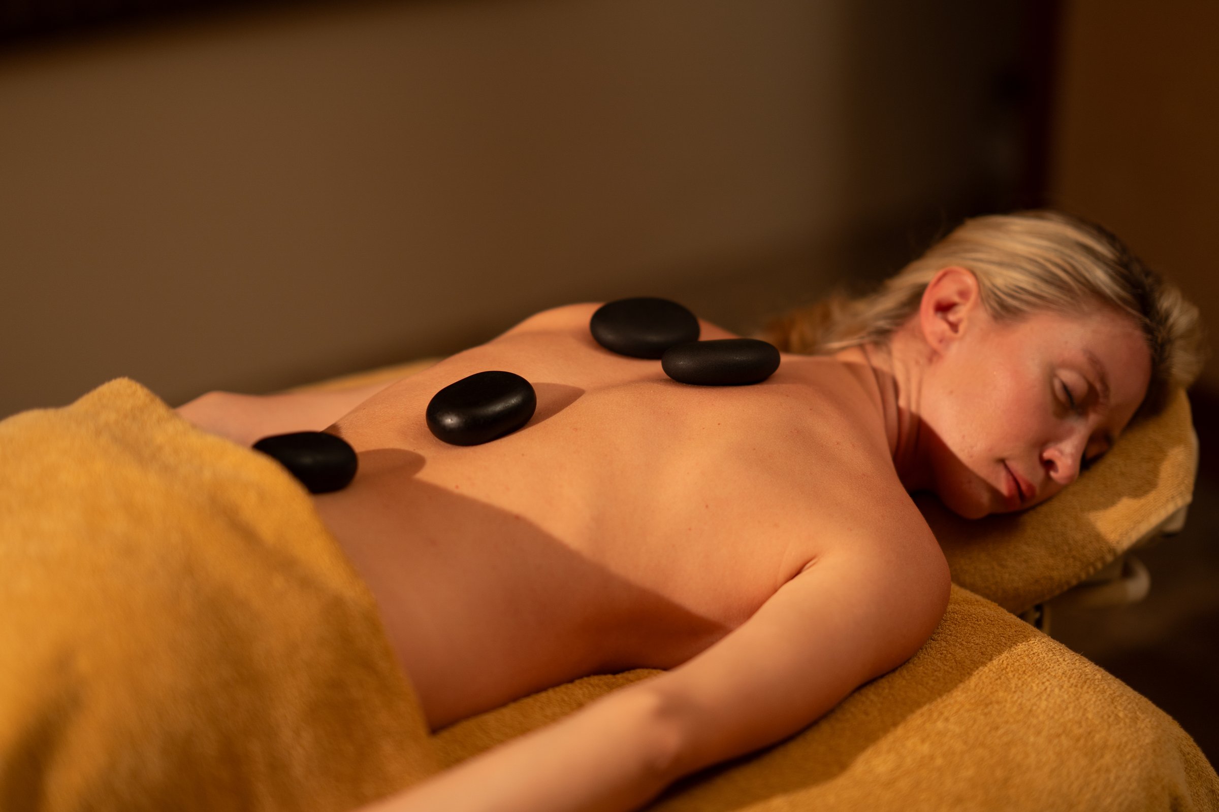 Woman relaxing during a hot stone massage therapy session in a warm and calming spa environment