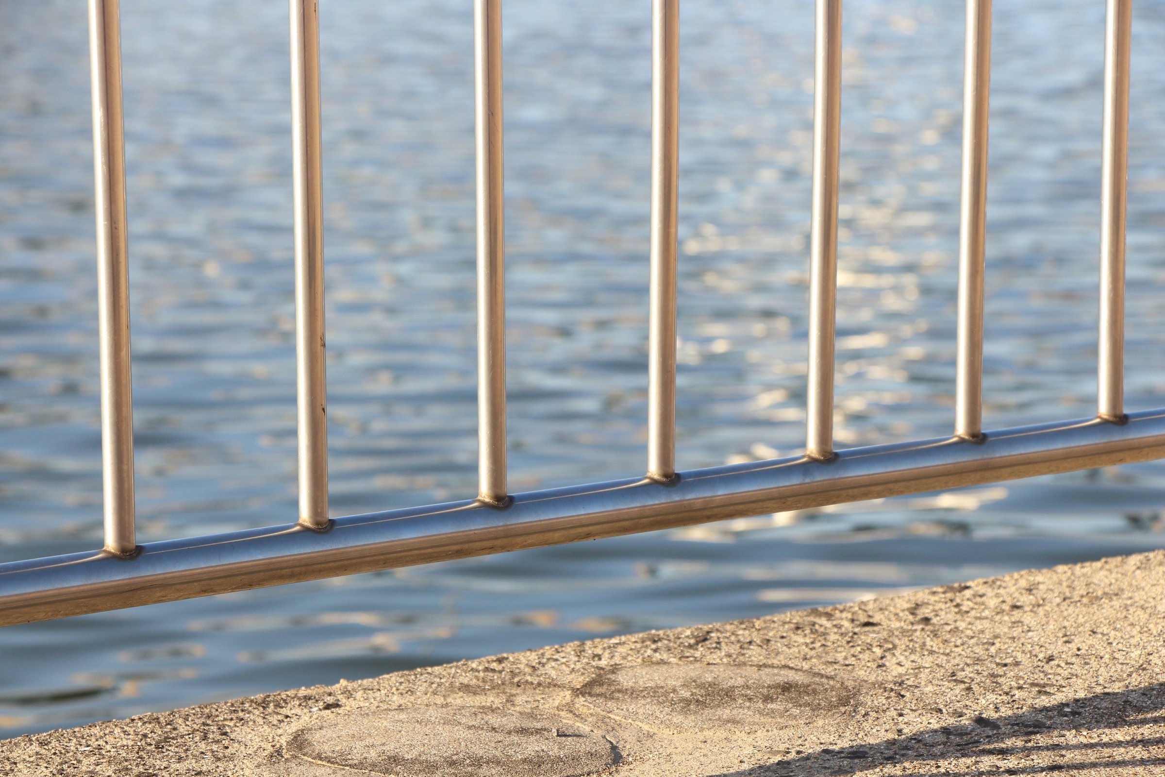 The strong metal handrail, which shows the importance of waterside safety measures, is softly illuminated, emphasizing its texture and role. It is safe to view.