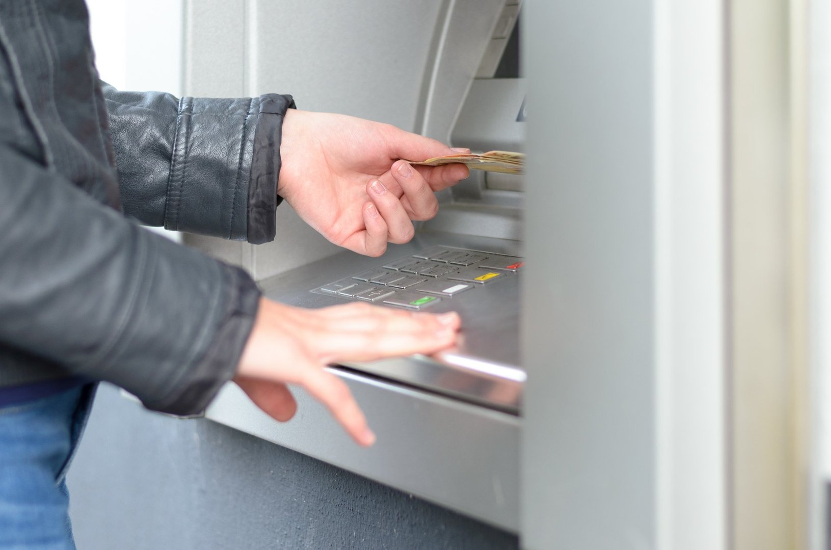 Young woman making a banking withdrawal at an outdoor ATM standing waiting for the machine to dispense the cash or banknotes, close up side view of her hands