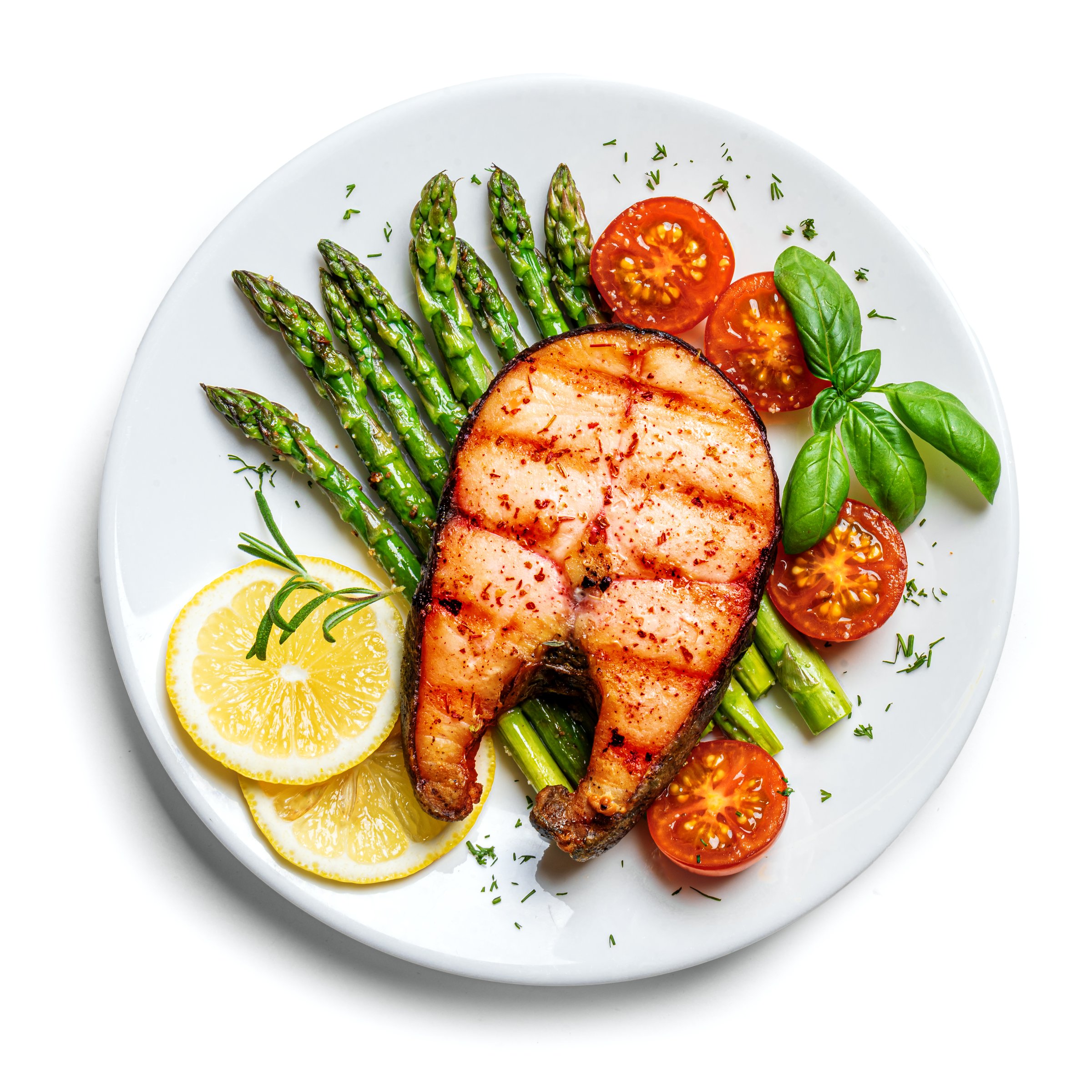 Grilled salmon steak with green asparagus, tomatoes and lemon slices served on white plate isolated on white background, top view. Balanced healthy meal.