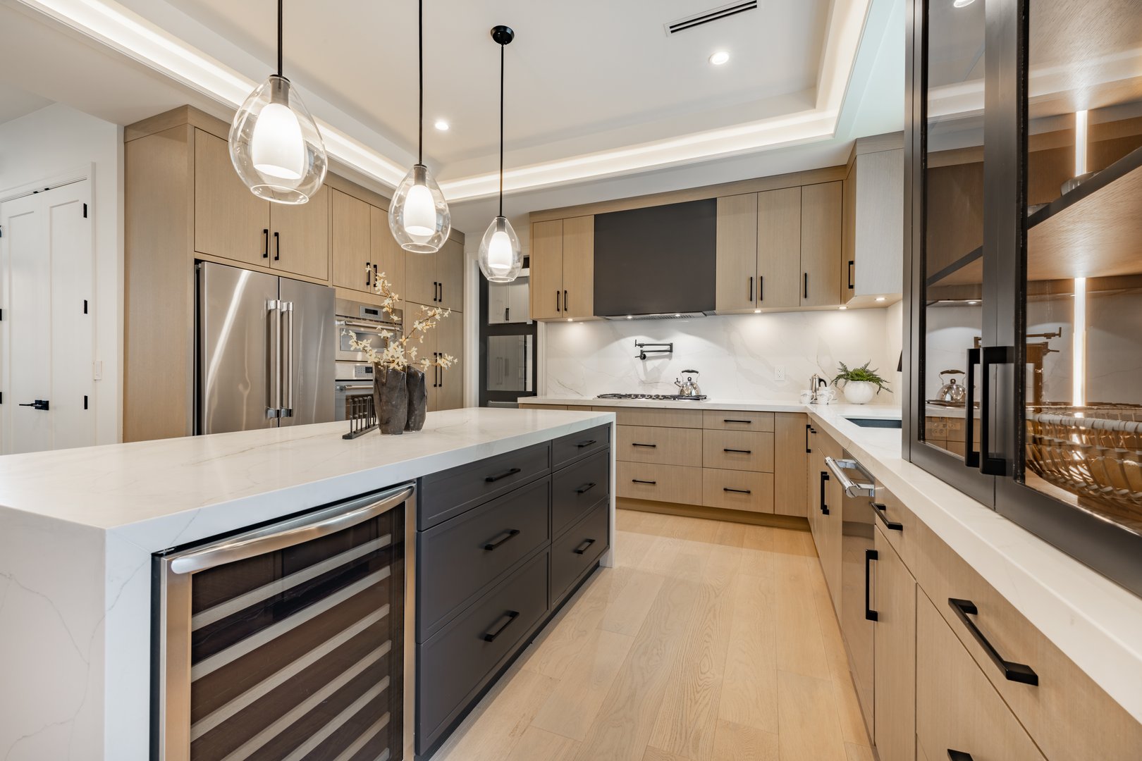 Kitchen interior with bar stools white countertops wooden cabinets pendant lighting extra kitchen sink glass cabinets hardwood floors stainless steel appliances window with coverings blinds drawn