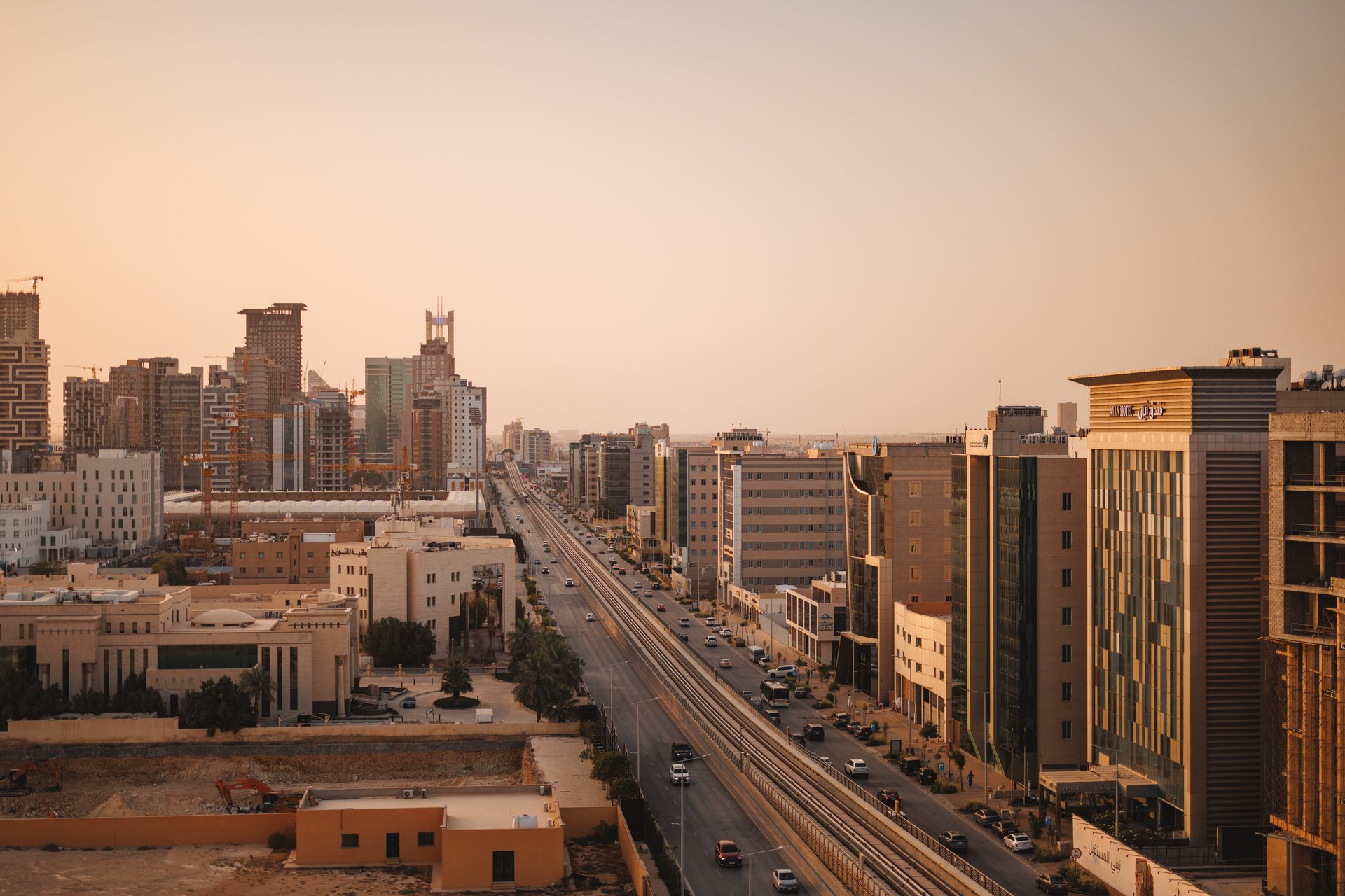 Aerial view of Riyadh cityscape featuring modern buildings, busy roads, and construction sites under a warm sunset. The image captures the dynamic urban development and architectural diversity of the city in a bustling environment.