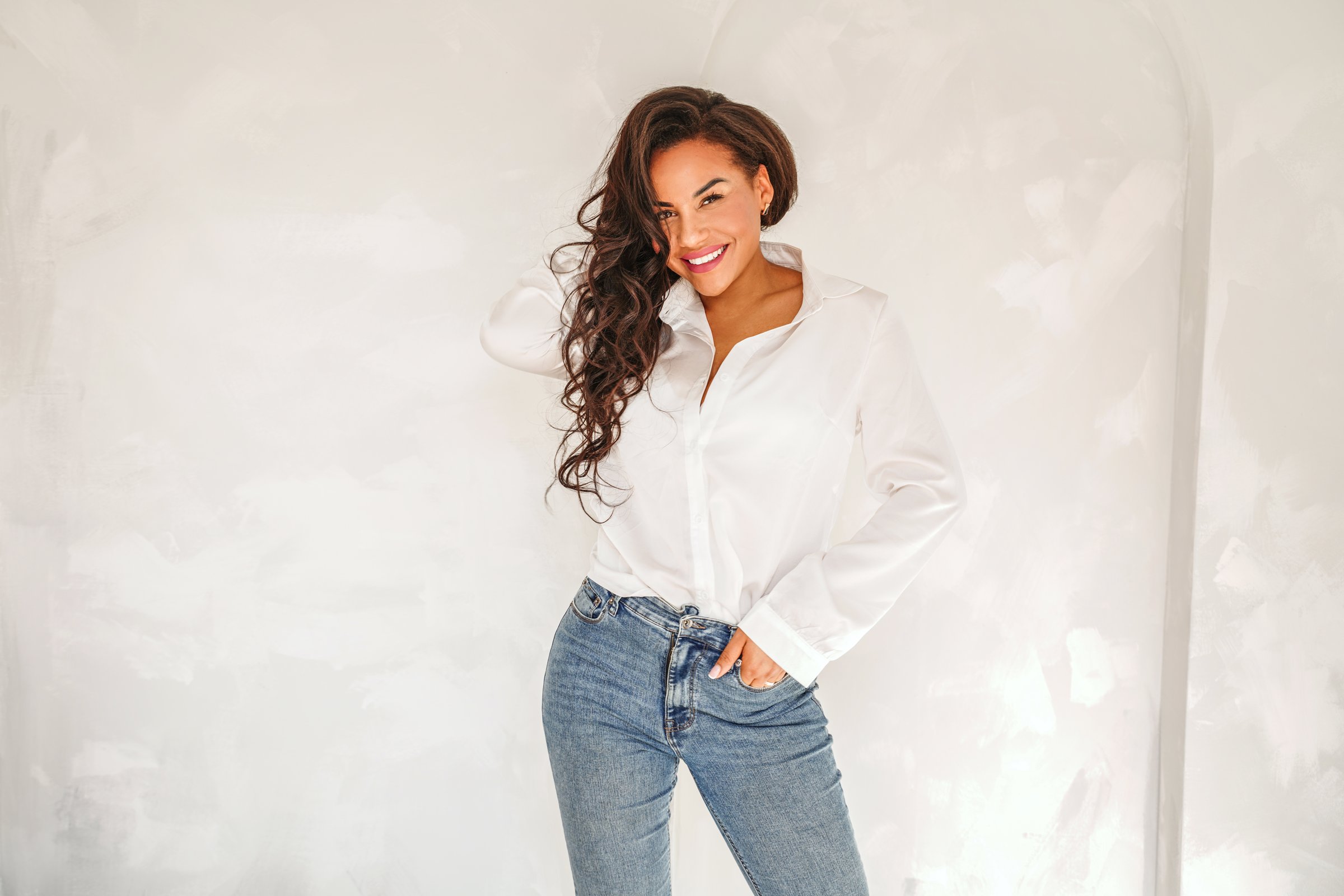Beautiful woman posing in white shirt and jeans, casual elegant look. Smiling attractive lady with long dark hair looking at the camera. A lot of copy space.