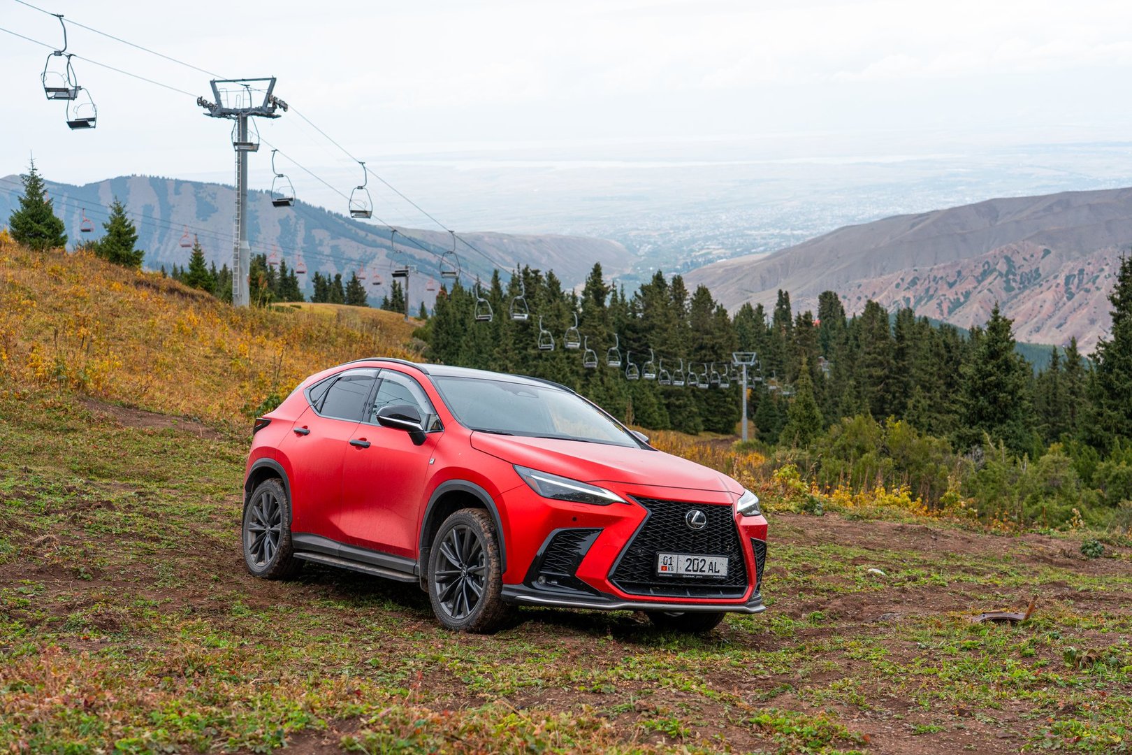 Bishkek, Kyrgyzstan - October 12, 2024: Front view of a red Lexus NX350 SUV parked on a grassy hill at a mountain resort with ski lift chairs