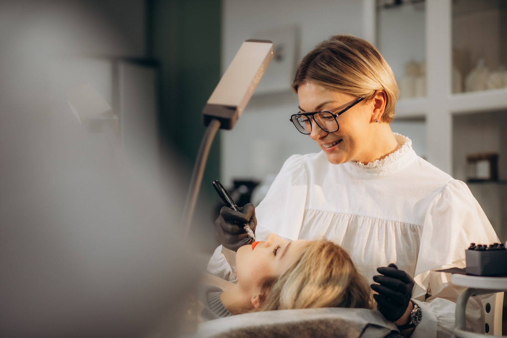 Professional permanent makeup artist and her client during lip blushing procedure.