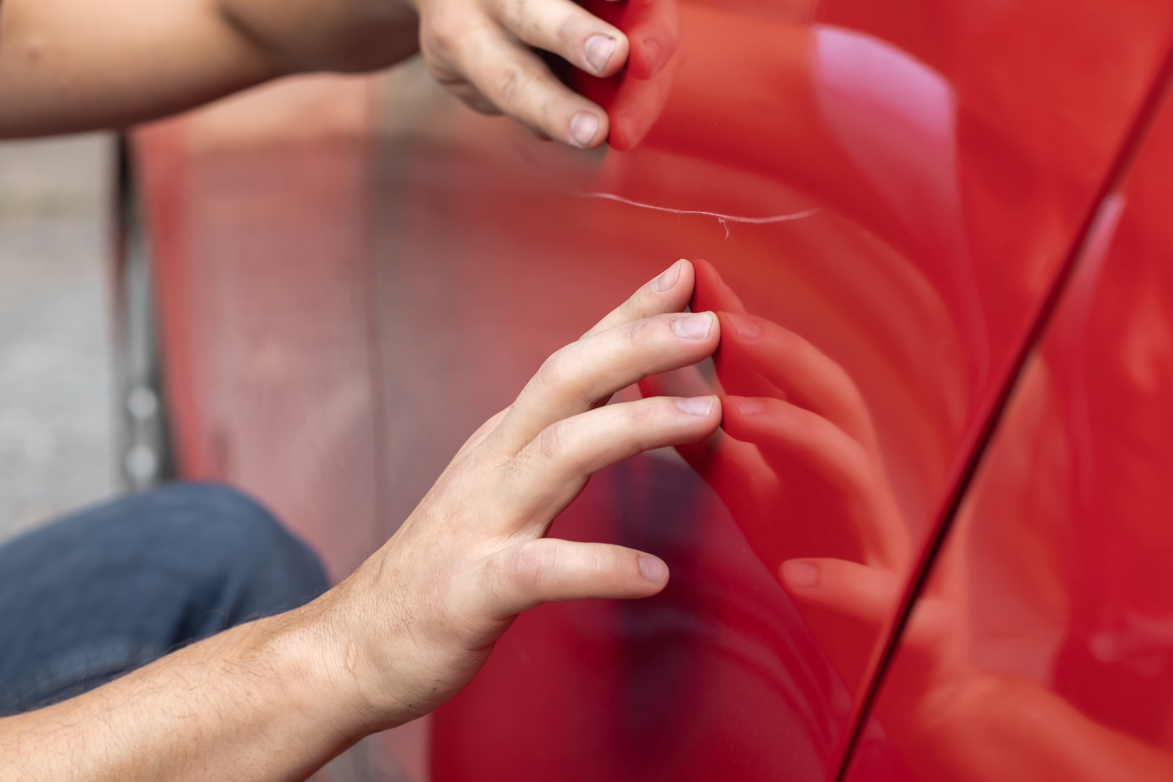 ropped image of a man's hands examining a scratch on his car