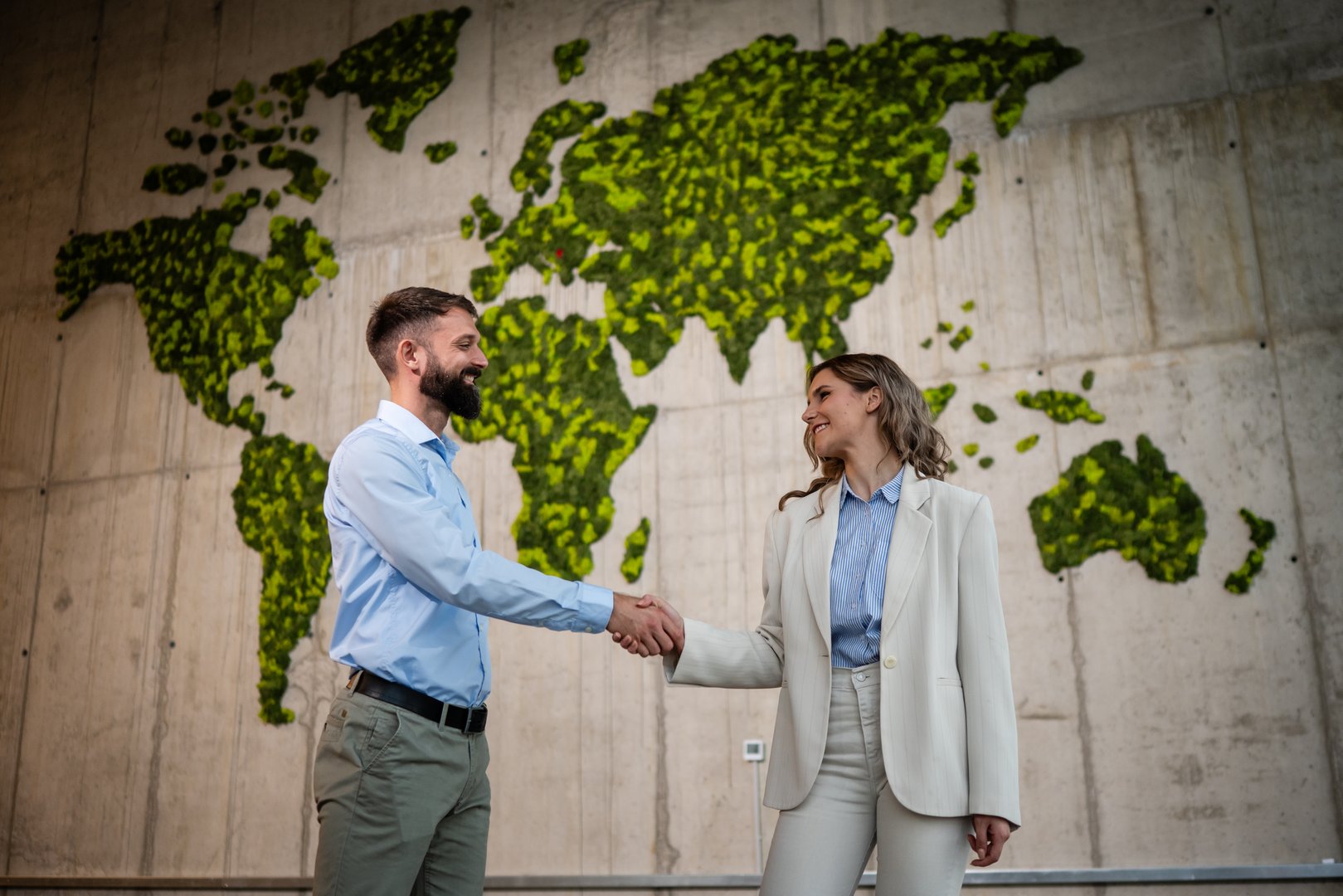 Businesspeople making a global partnership agreement. World map made of moss on wall representing environmental sustainability and eco-friendly business