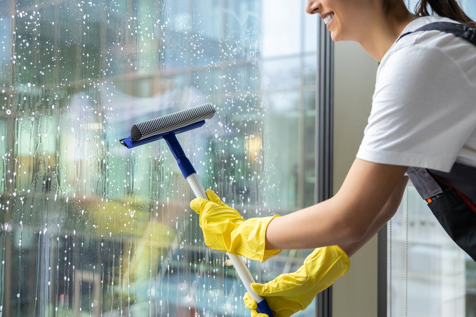Window cleaning. Woman in yellow gloves rubbing the window with the window washer