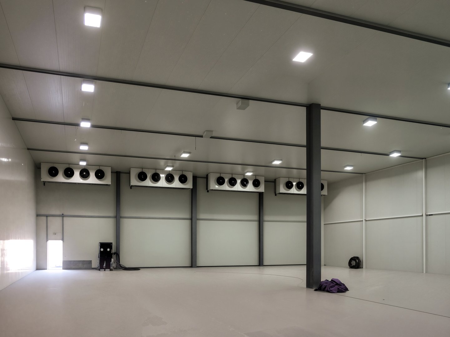 A spacious, brightly lit industrial cold storage room. The interior features multiple cooling units, clean walls, and a polished floor, creating a modern environment.