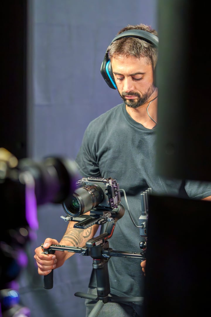 Young Male Camera Operator Using a Gimbal for Filming on a Professional TV Set with Headphones