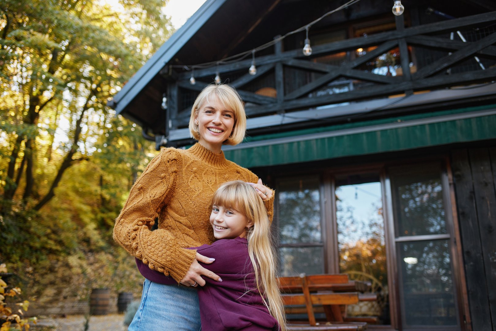 Mother and daughter smiling while embracing outdoors in autumn