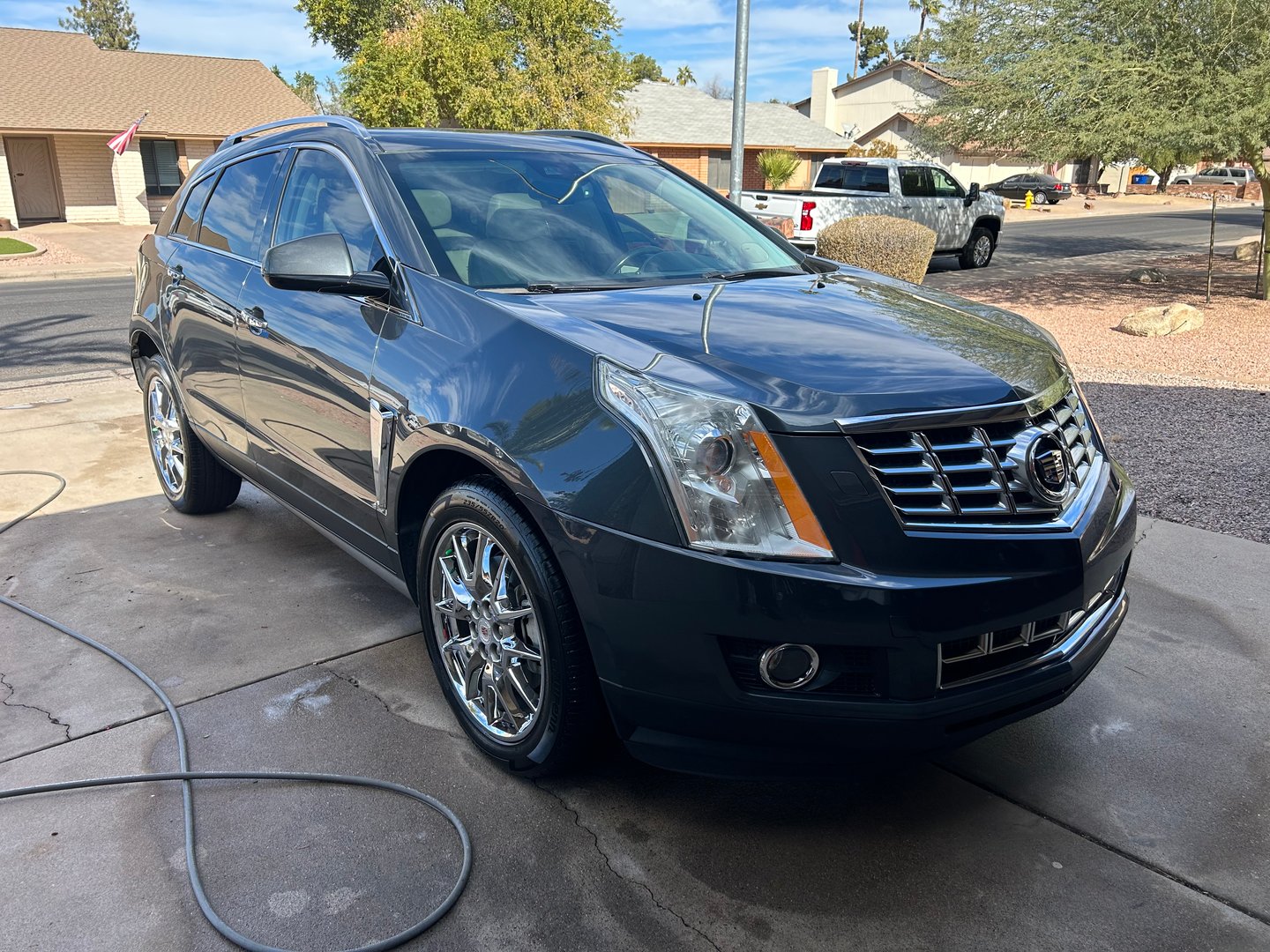 A shiny black SUV parked in a driveway with chrome wheels and a hose on the ground, set in a suburban neighborhood.