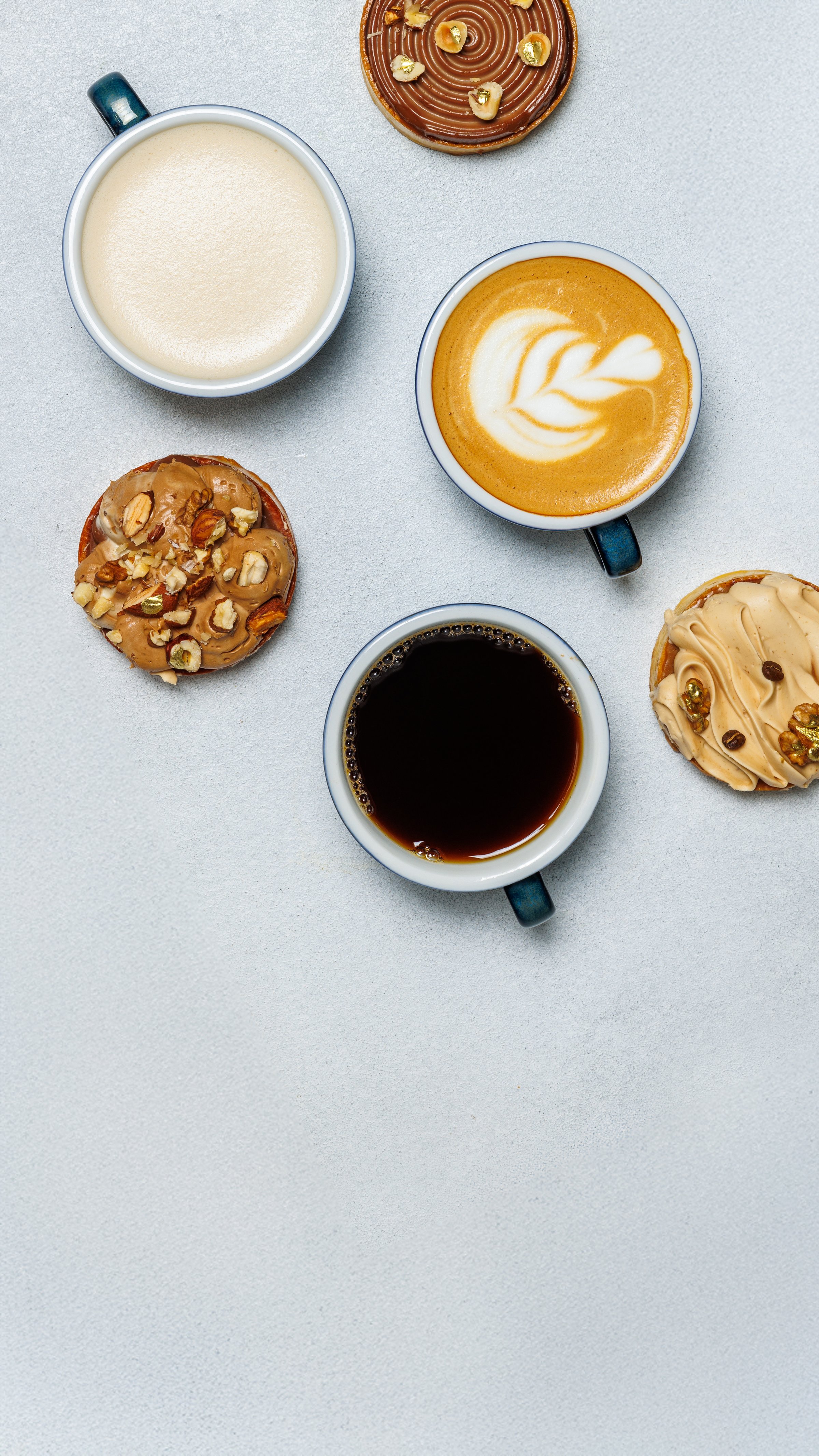 A flat lay of various coffee beverages and pastries on a light gray surface. Theme for a menu for cafes and restaurants. Light background. Cappuccino, americano, latte and desserts. Copy space