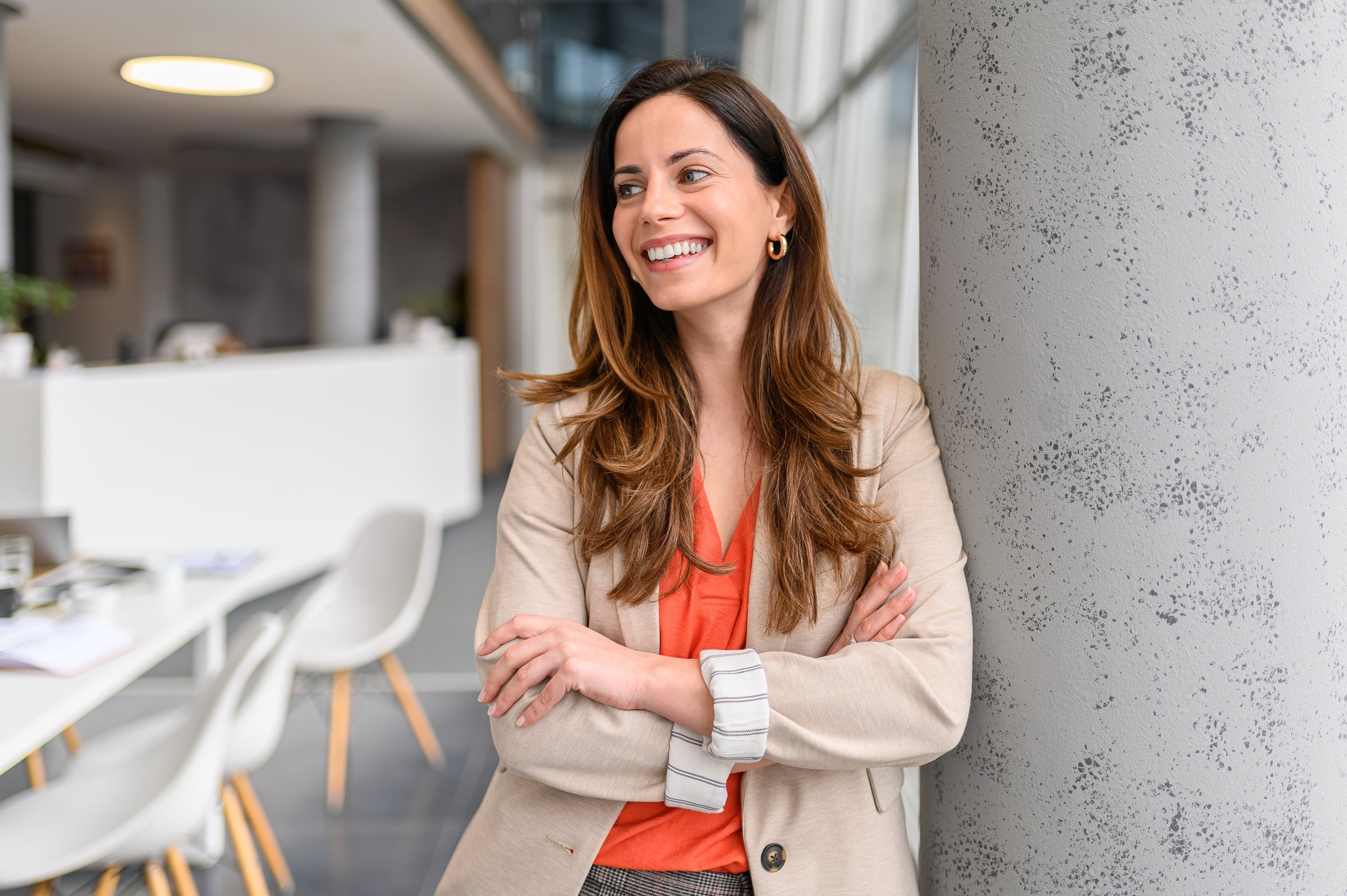 Portrait of confident businesswoman with arms crossed smiling and looking away while standing by column in office