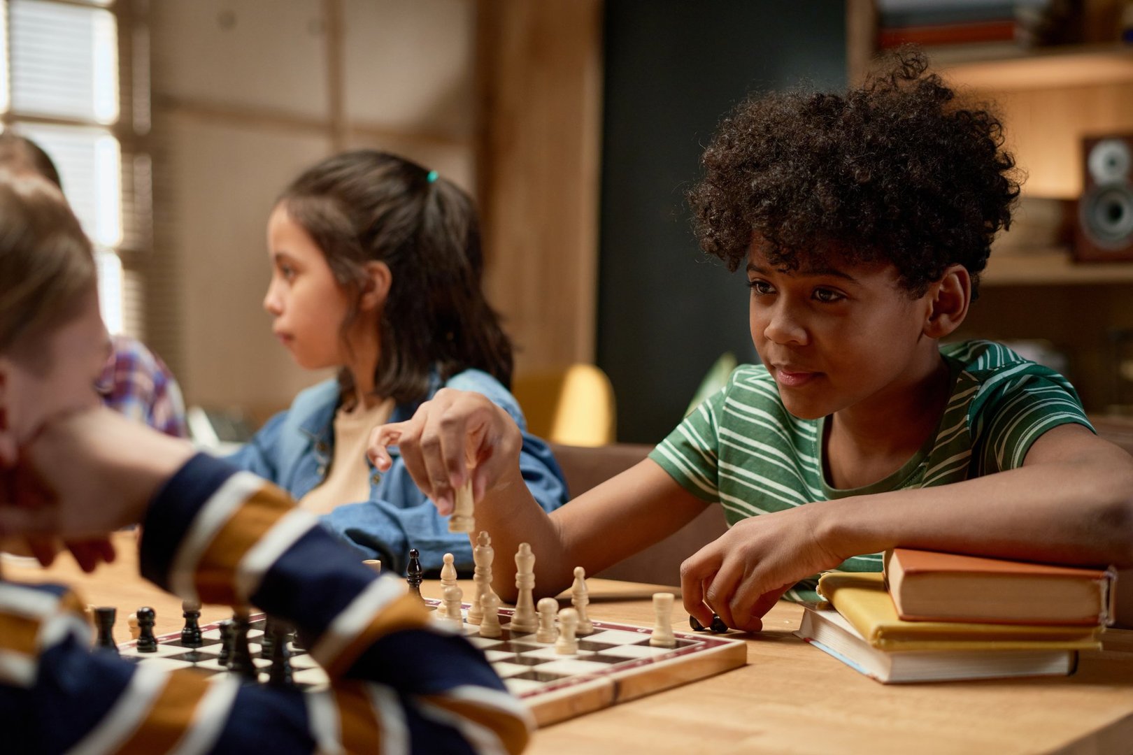 Youthful African American boy looking at checkmate sitting in front of him and holding white pawn or other figurine over chess board