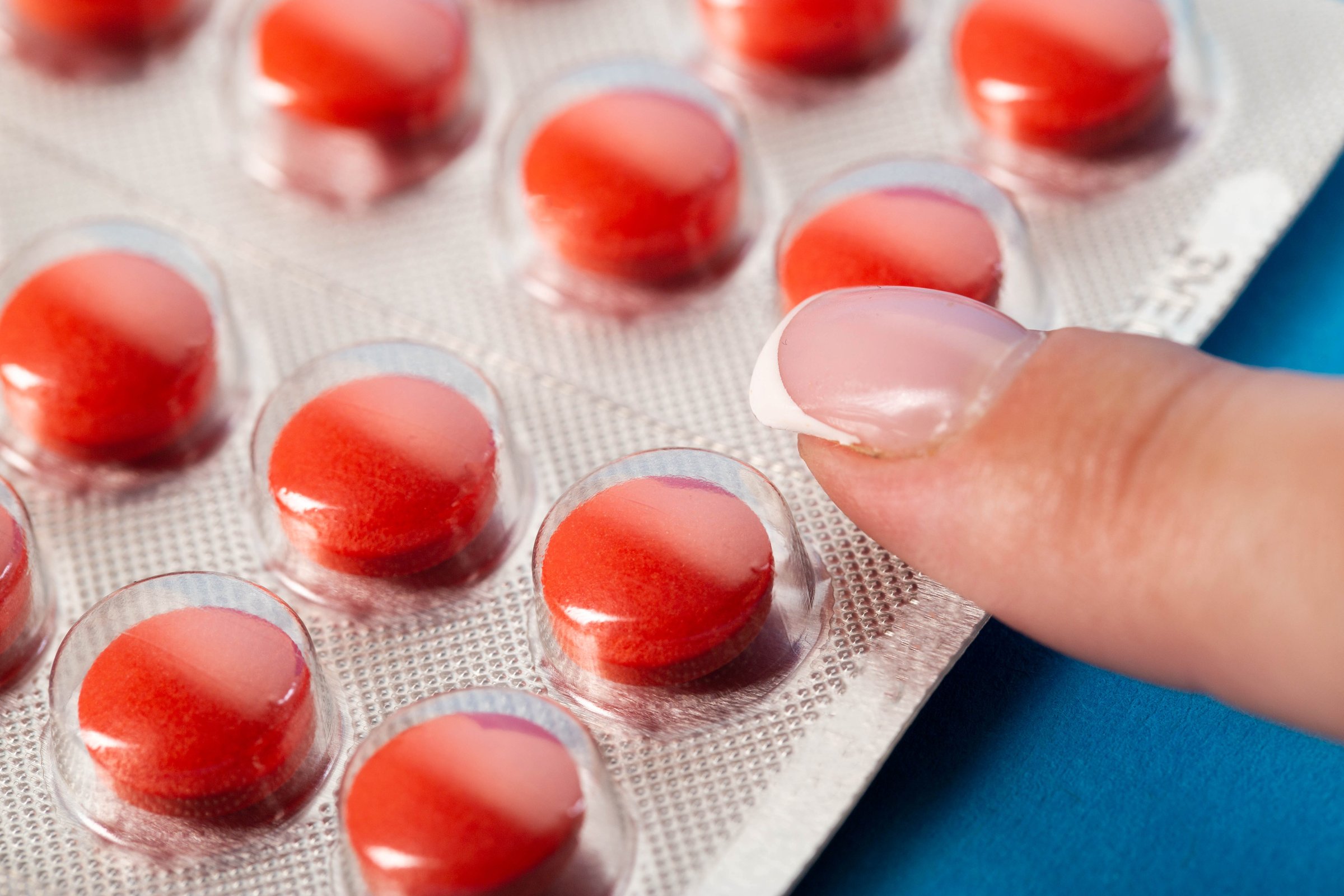 Woman's finger with manicure on a blister with red pills. Concept of nootropic pills, sedative pills